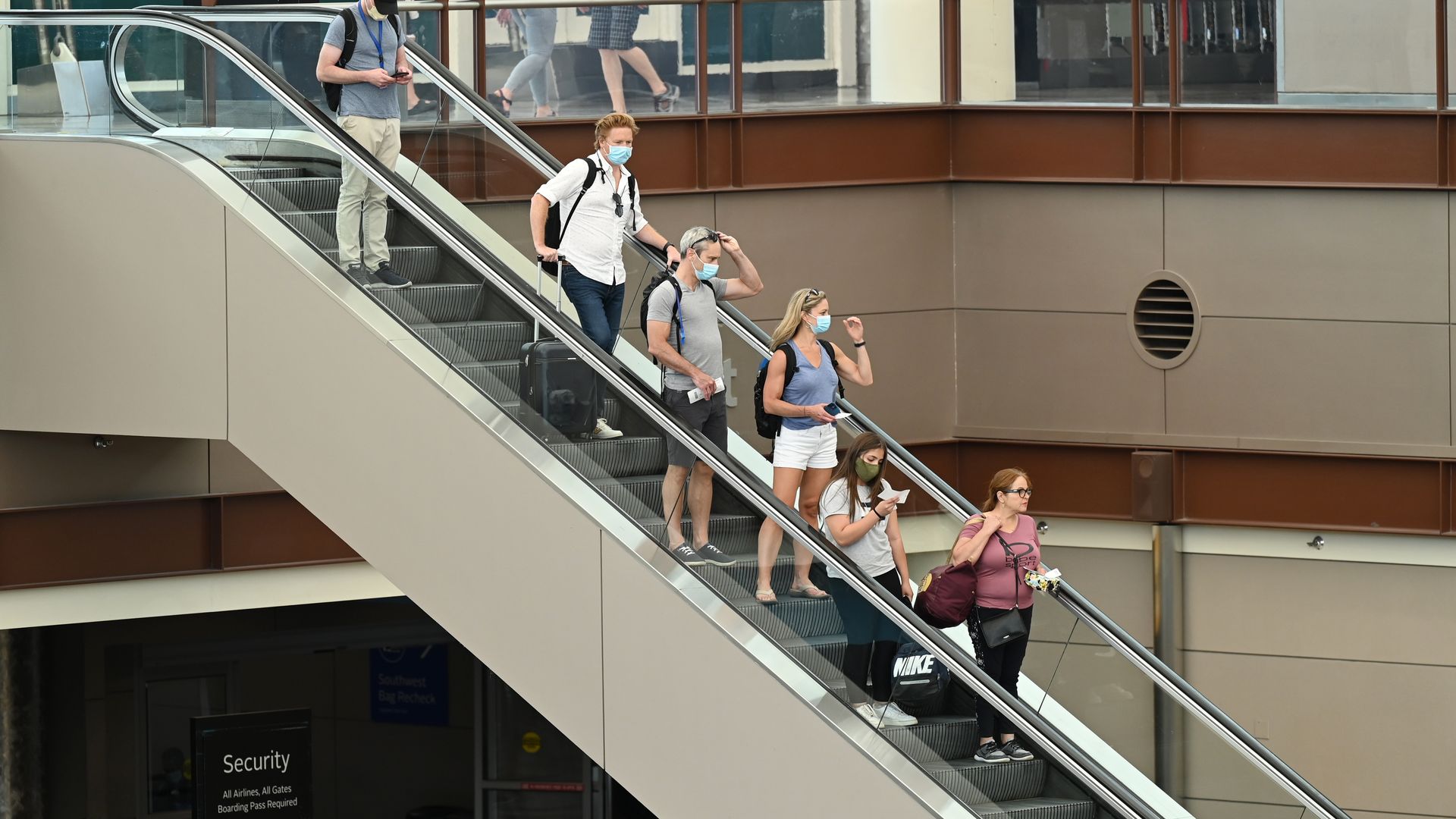 A photo of passengers riding down an escalator with face masks on