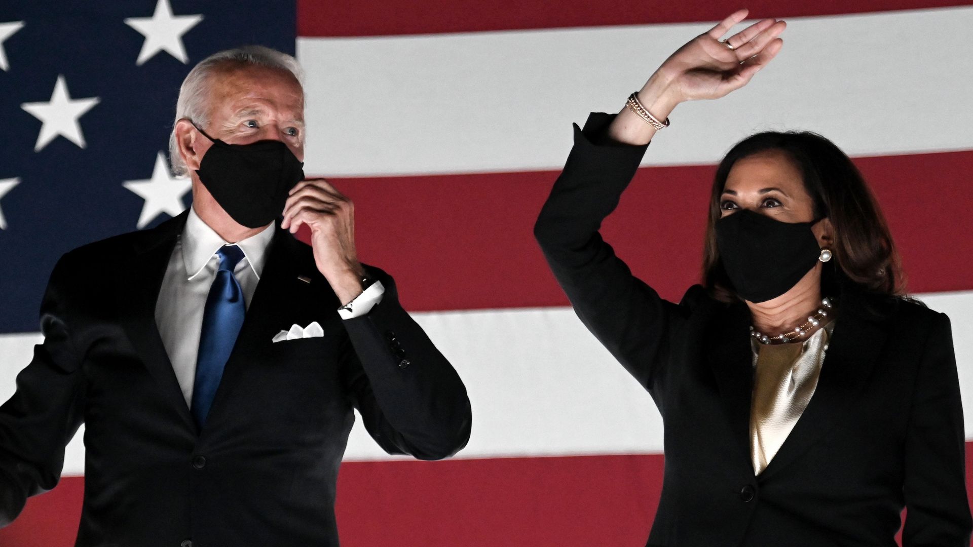 Harris and Biden stand next to each other in front of an American flag 