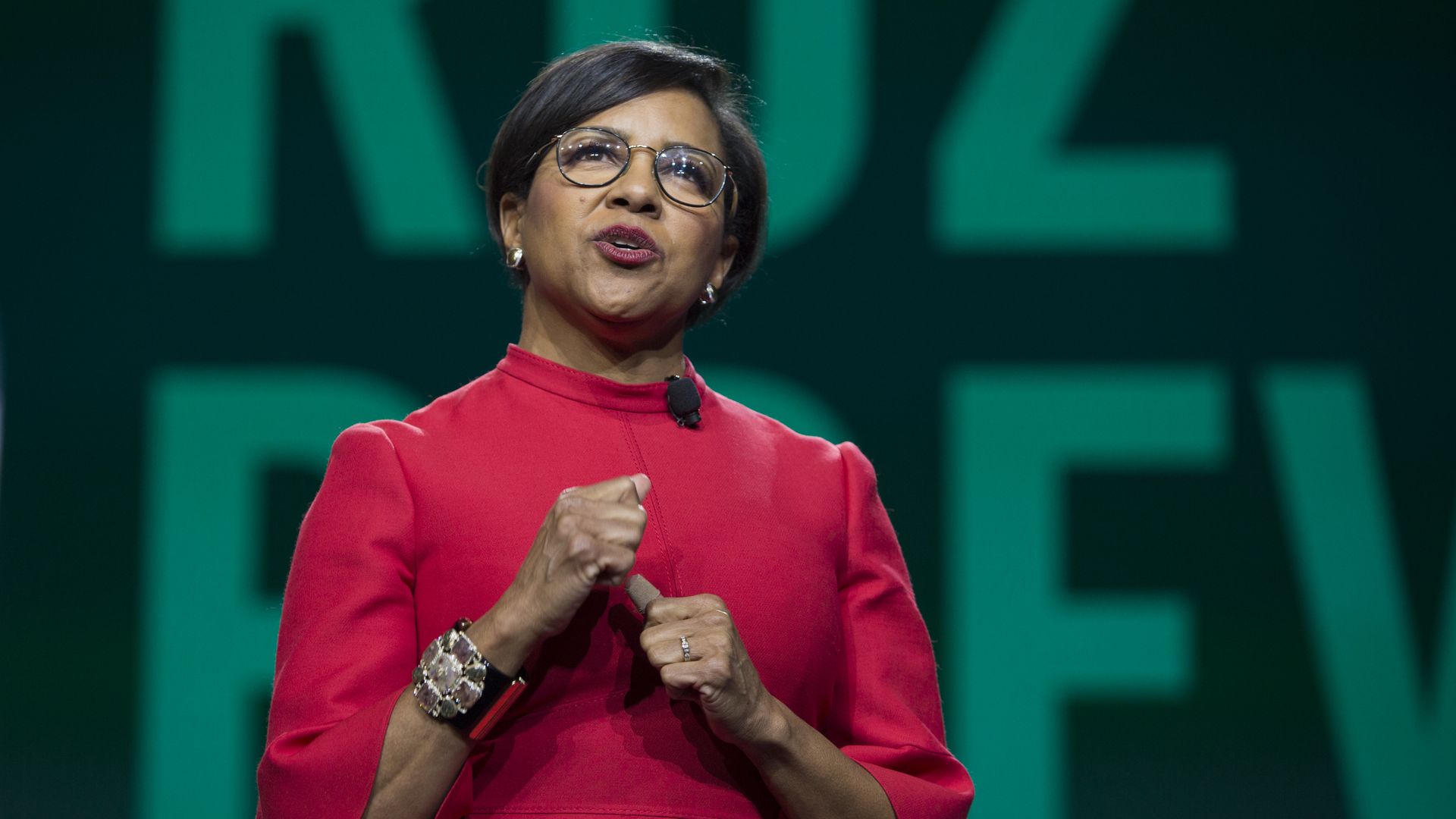 photo of a woman in glasses and a red dress against a screen as she's presenting