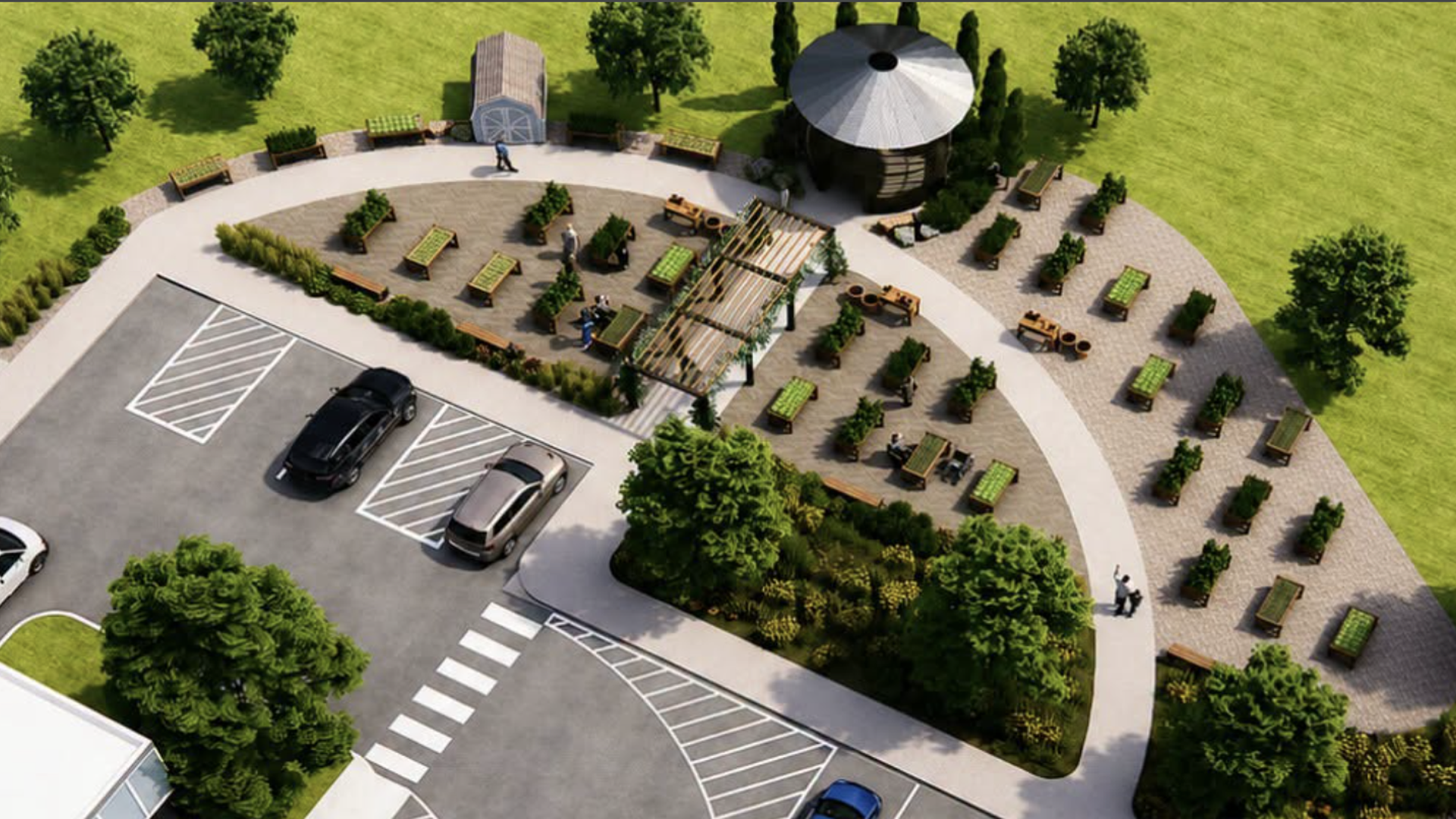 Aerial view of a park-like space: circular paved plaza with benches, planters, and a pergola, plus a small round shed. Green lawns and trees surround the area, with a parking lot nearby.