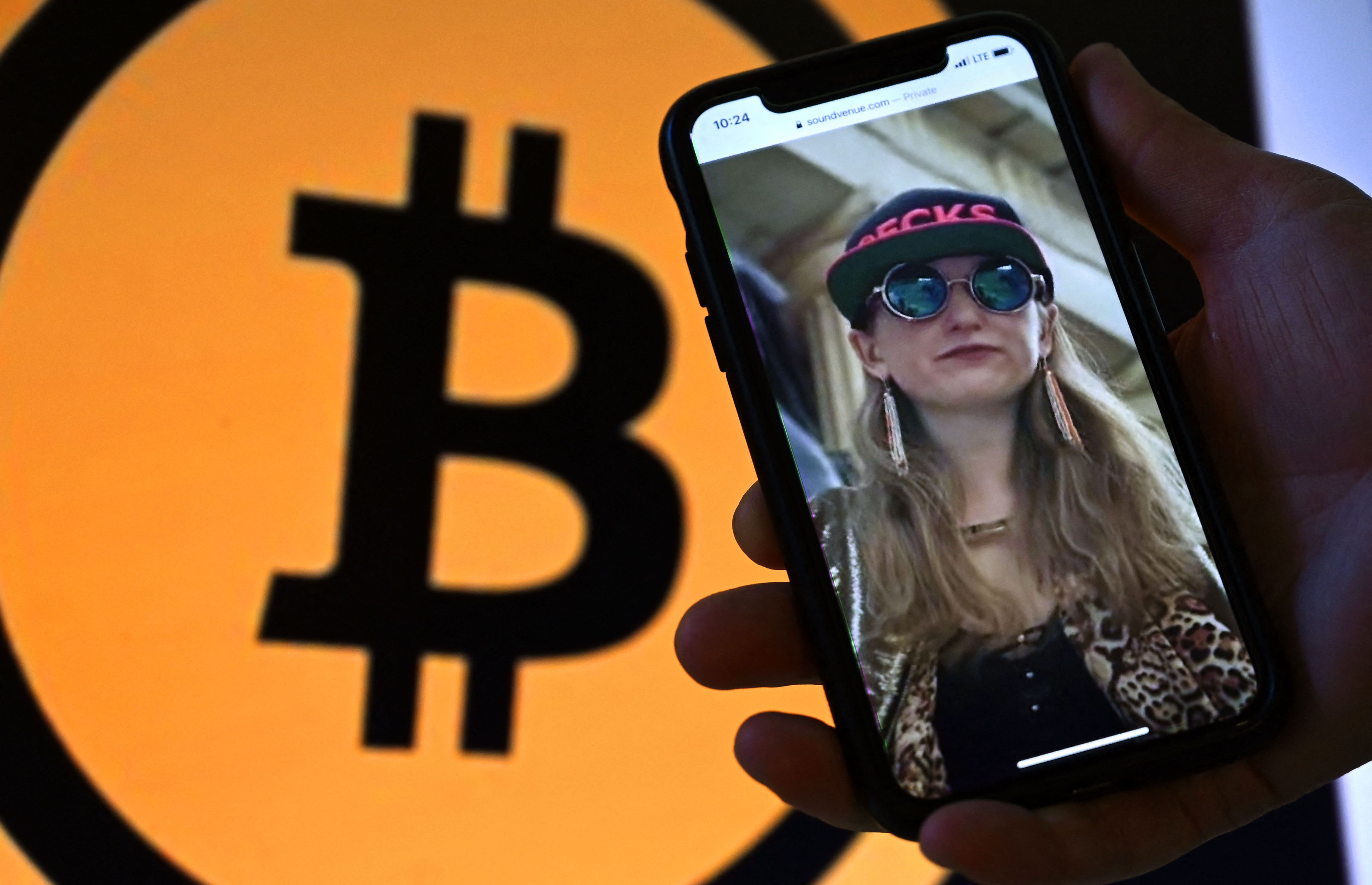 This illustration photo shows Heather Morgan, also known as "Razzlekhan," on a phone in front of the Bitcoin logo displayed on a screen, in Washington, DC, February 9, 2022.