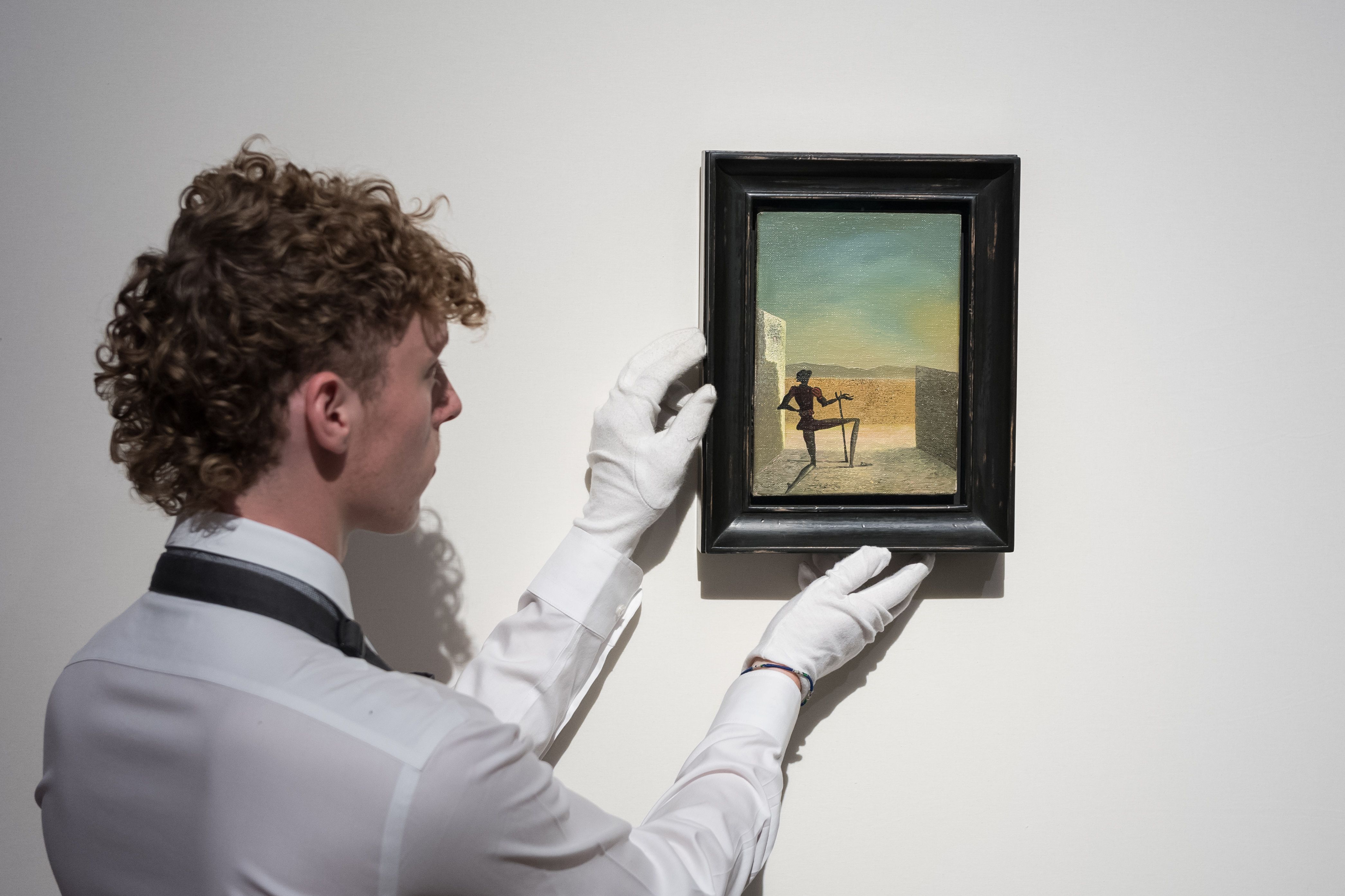 An art handler holds a painting titled 'Le spectre de Vermeer de Delft' by Salvador Dali in London.