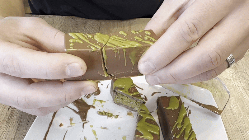 A person splits apart a chocolate bar to show pistachio cream and kunafe inside.