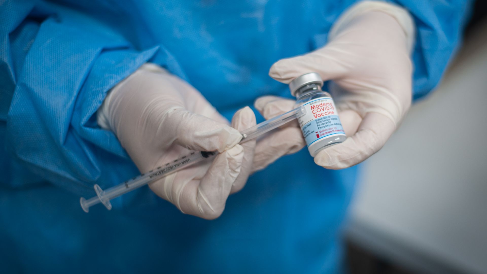 Picture of gloved hands holding a syringe and a vial of the Moderna vaccine