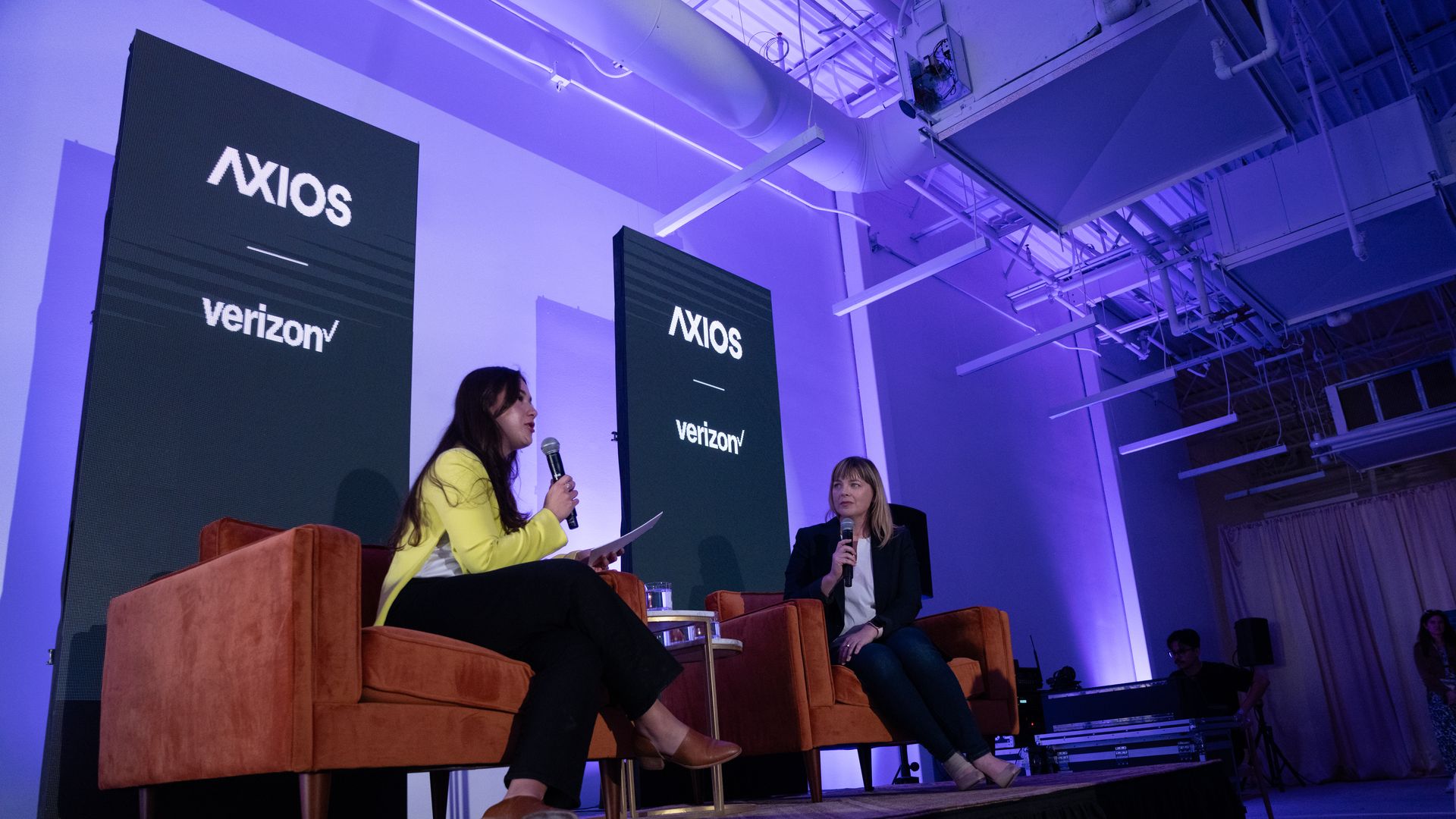 Two people sit on chairs holding mics