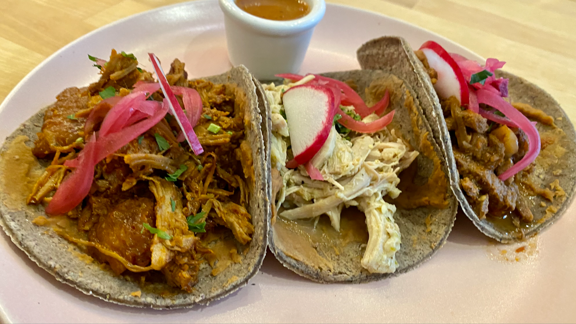 Three tacos on tortillas that are blue in color with meats and pickled onions piled on top.