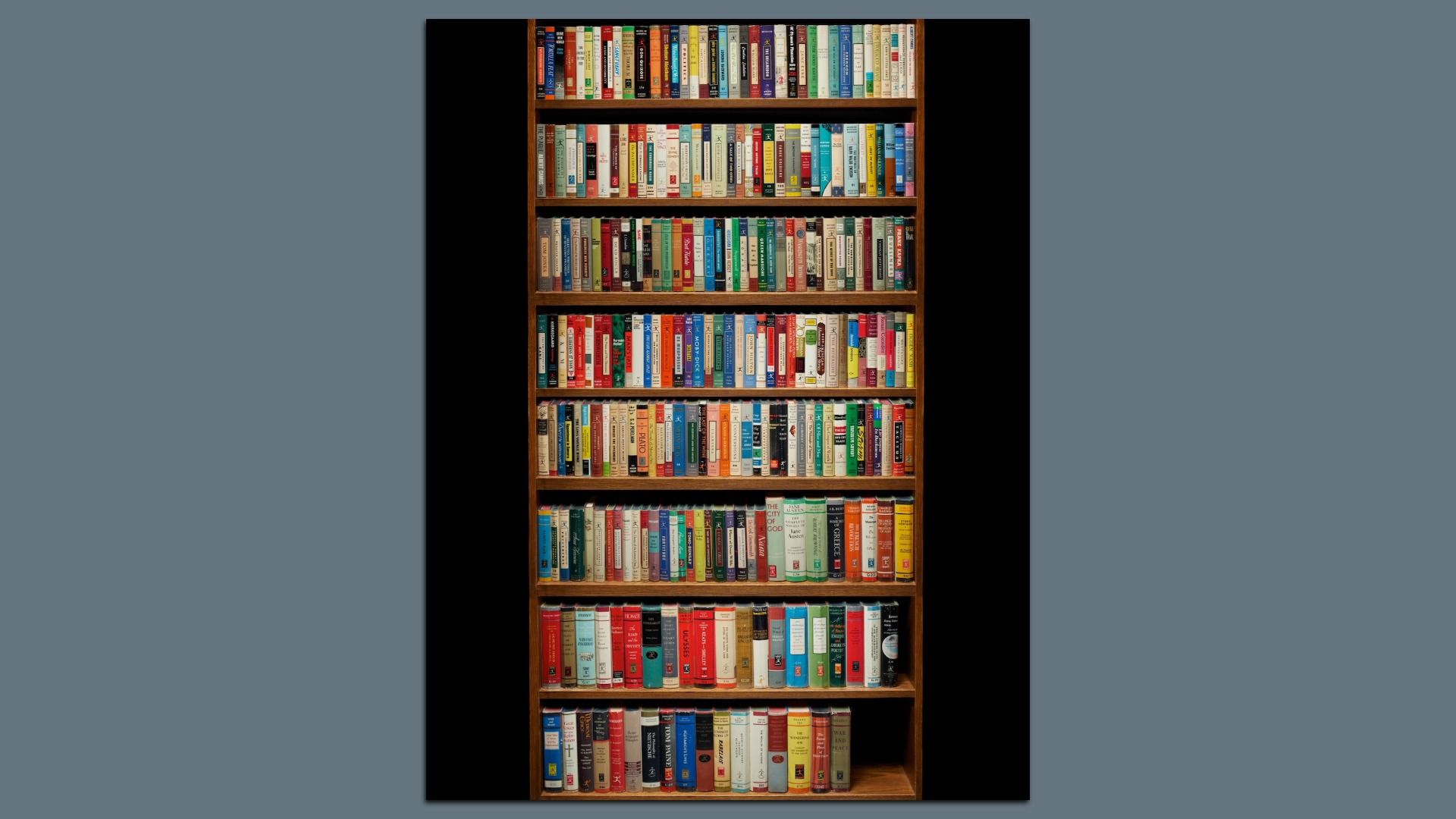 Wooden bookshelf with seven shelves filled with colorful hardcover and paperback books of various sizes, arranged vertically against a dark background.