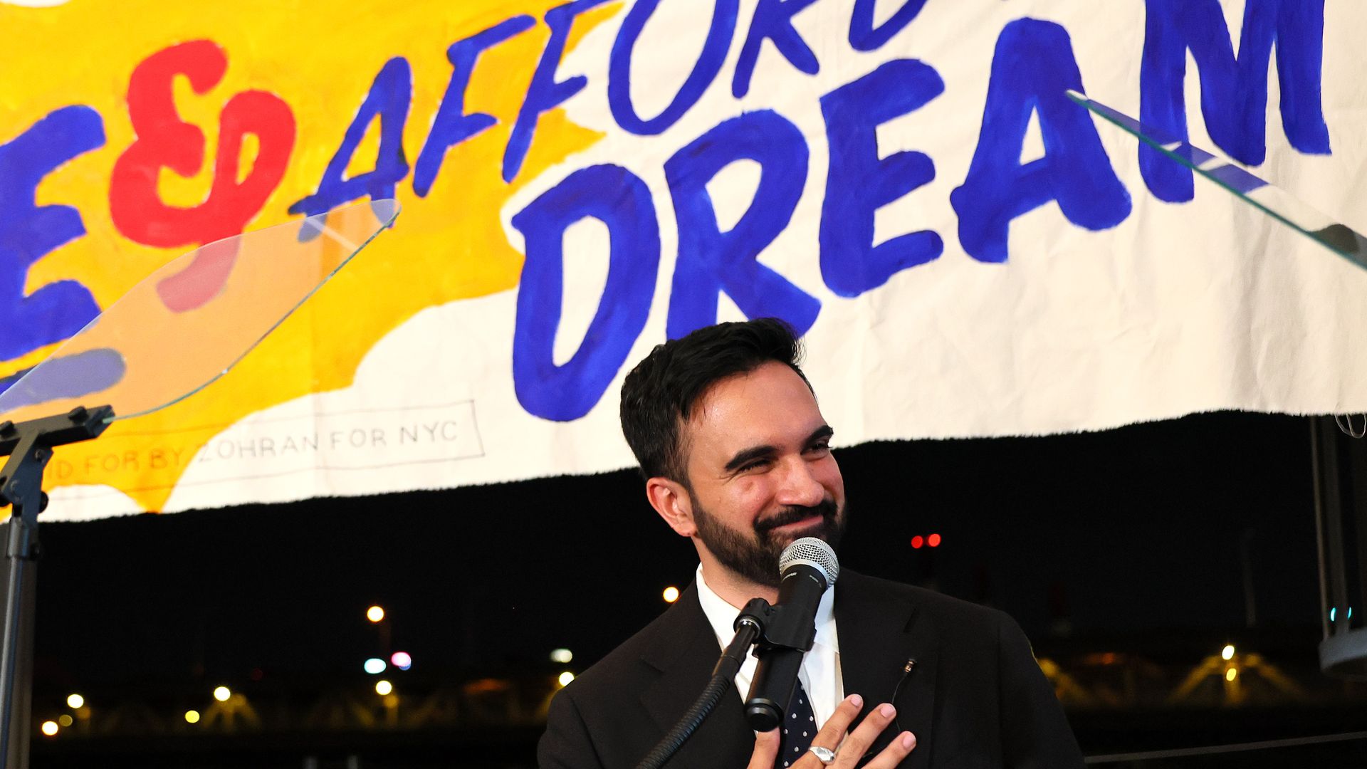 Mamdani behind a microphone and in front of a sign that reads "afford to dream." 
