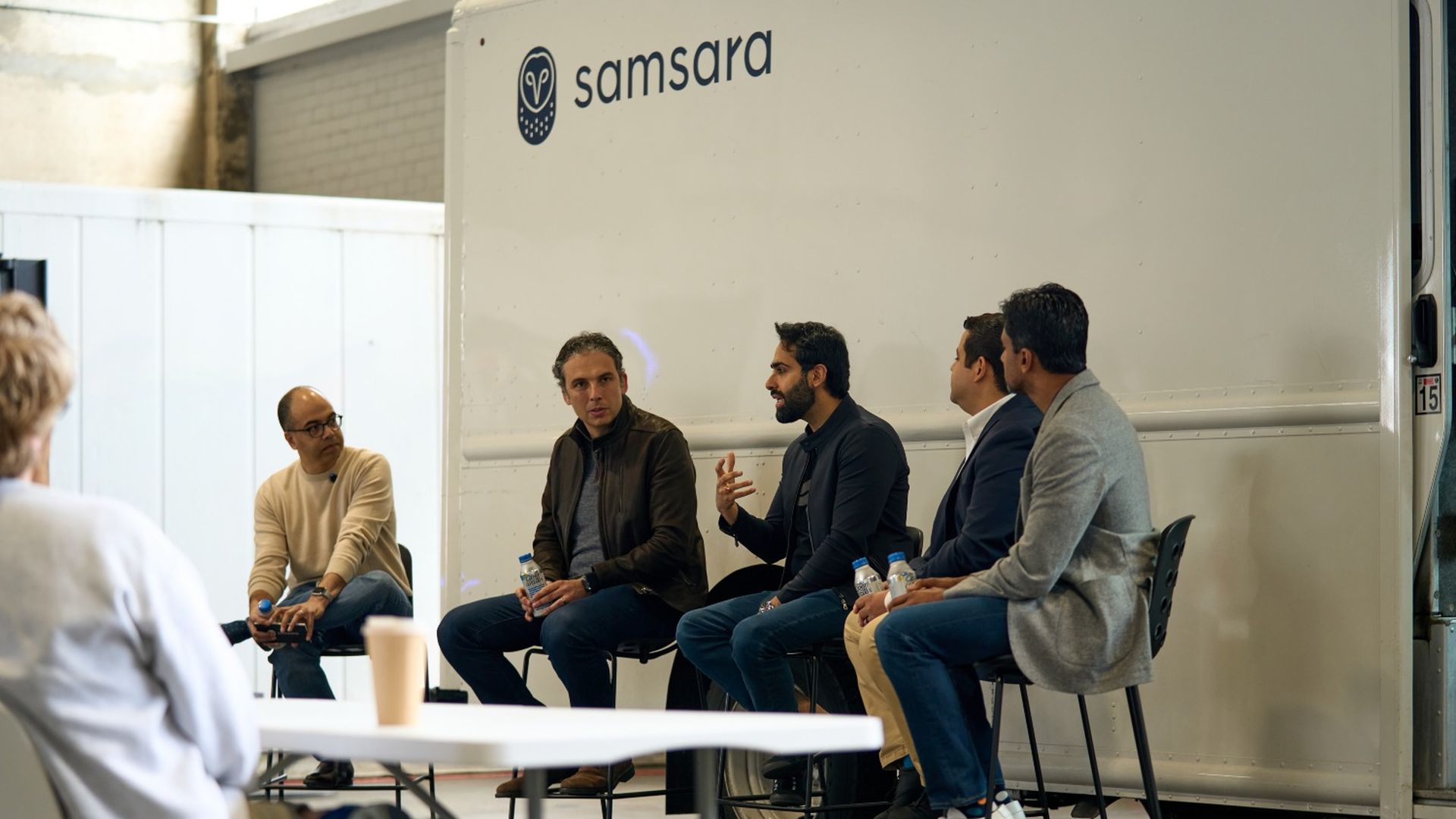 A group of men participate in a panel talk seated in front of a Samsara-branded truck.