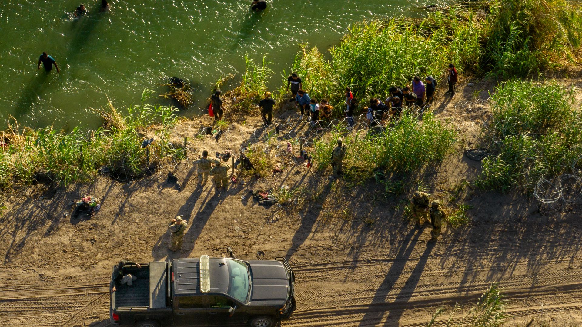  In an aerial view, migrants seeking asylum receive instructions from law enforcement officers after crossing the Rio Grande river into the United States 