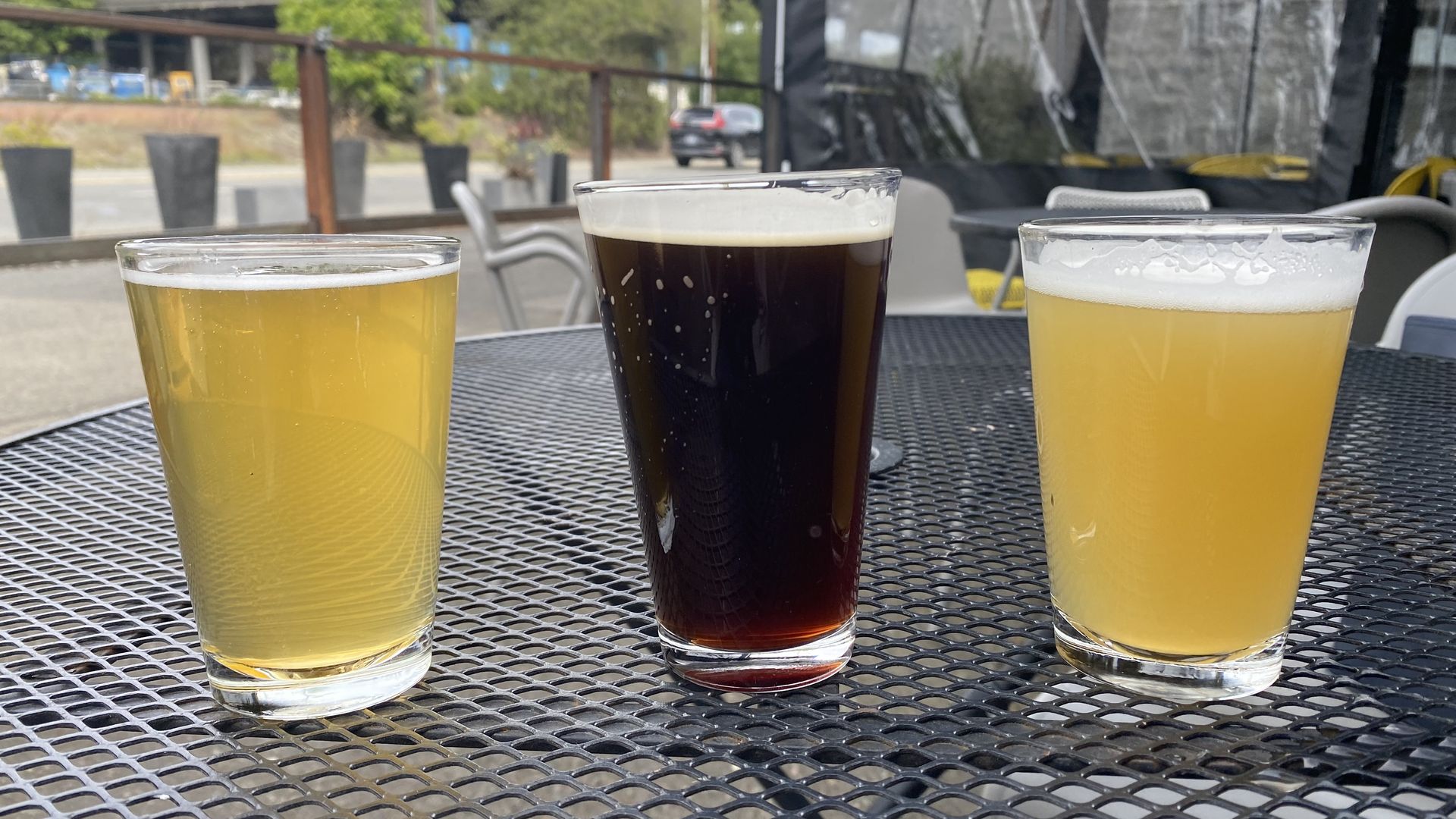 Three beers sitting on an outdoor table -- two lighter, one brown. 