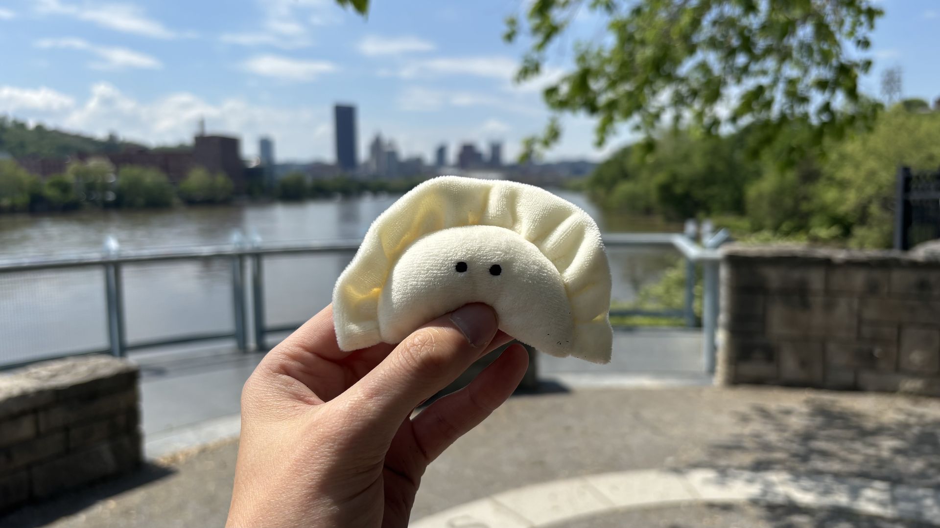 Nebby the pierogi mascot at an undisclosed location in Pittsburgh, looking out on the water and Downtown in the distance