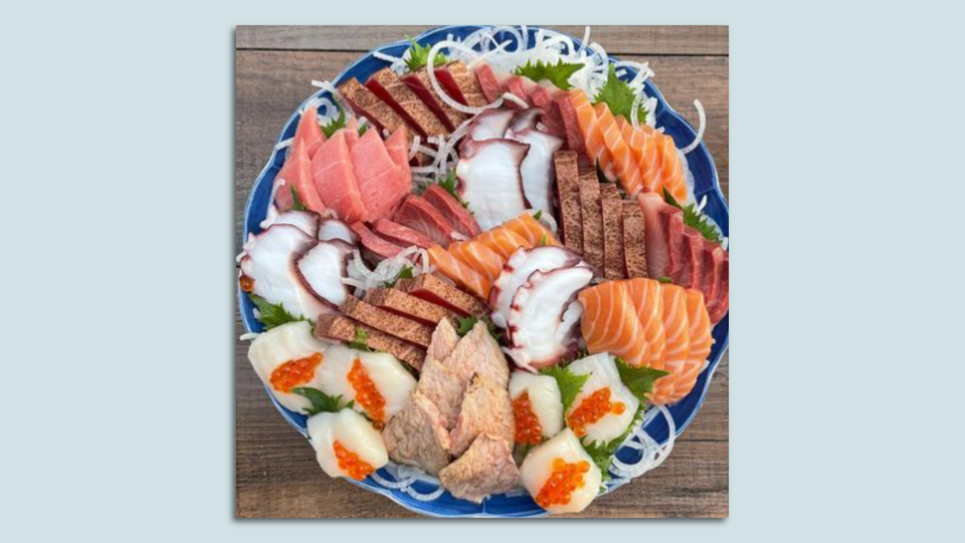 A platter of sashimi on a blue plate, shown in a photo mounted on a blue background. 