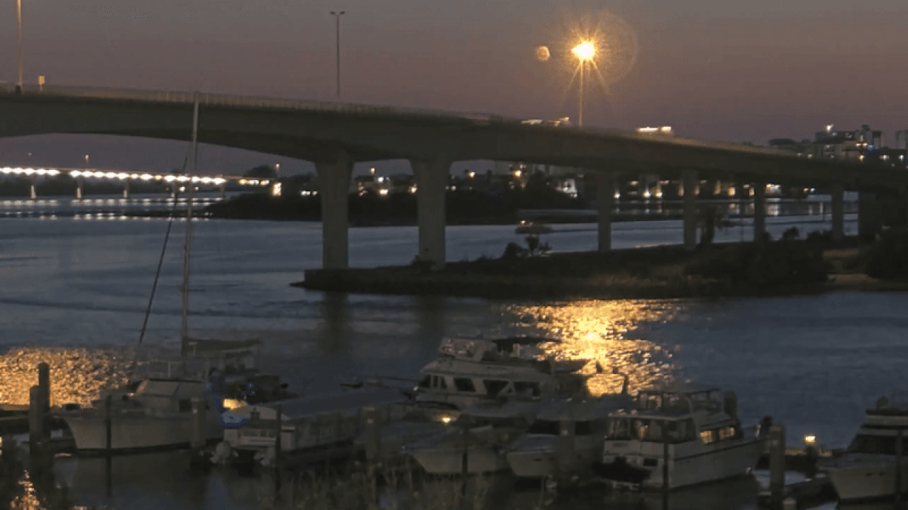 A gif of a harbor at dusk showing a boat speeding up behind another boat and ramming into it. The boats are both near a bridge spanning a body of water. A marina with yachts and sailboats can be seen in the foreground.
