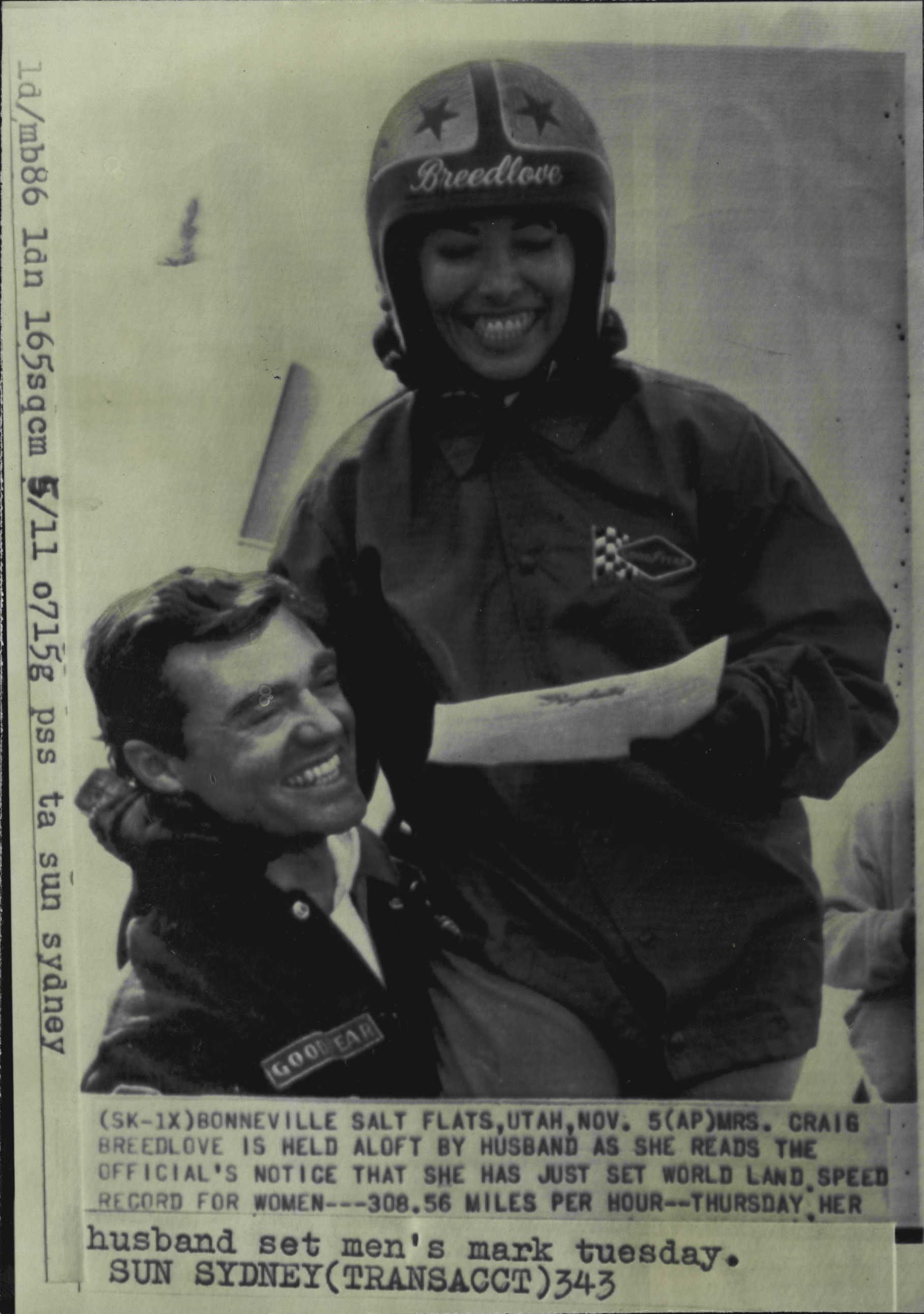 a woman in a helmet is hoisted up by a man as she holds a piece of paper.