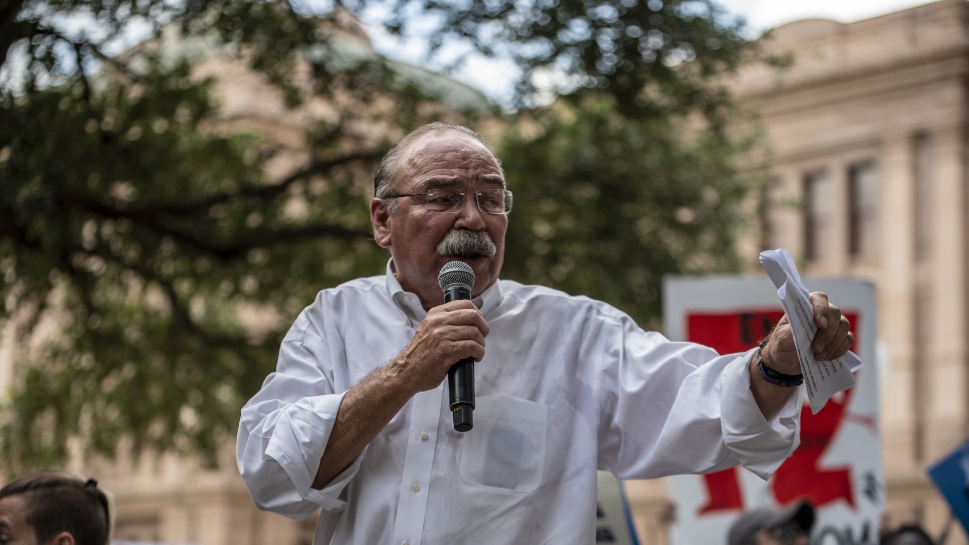 Gilberto Hinojosa holds a microphone, wearing a white shirt