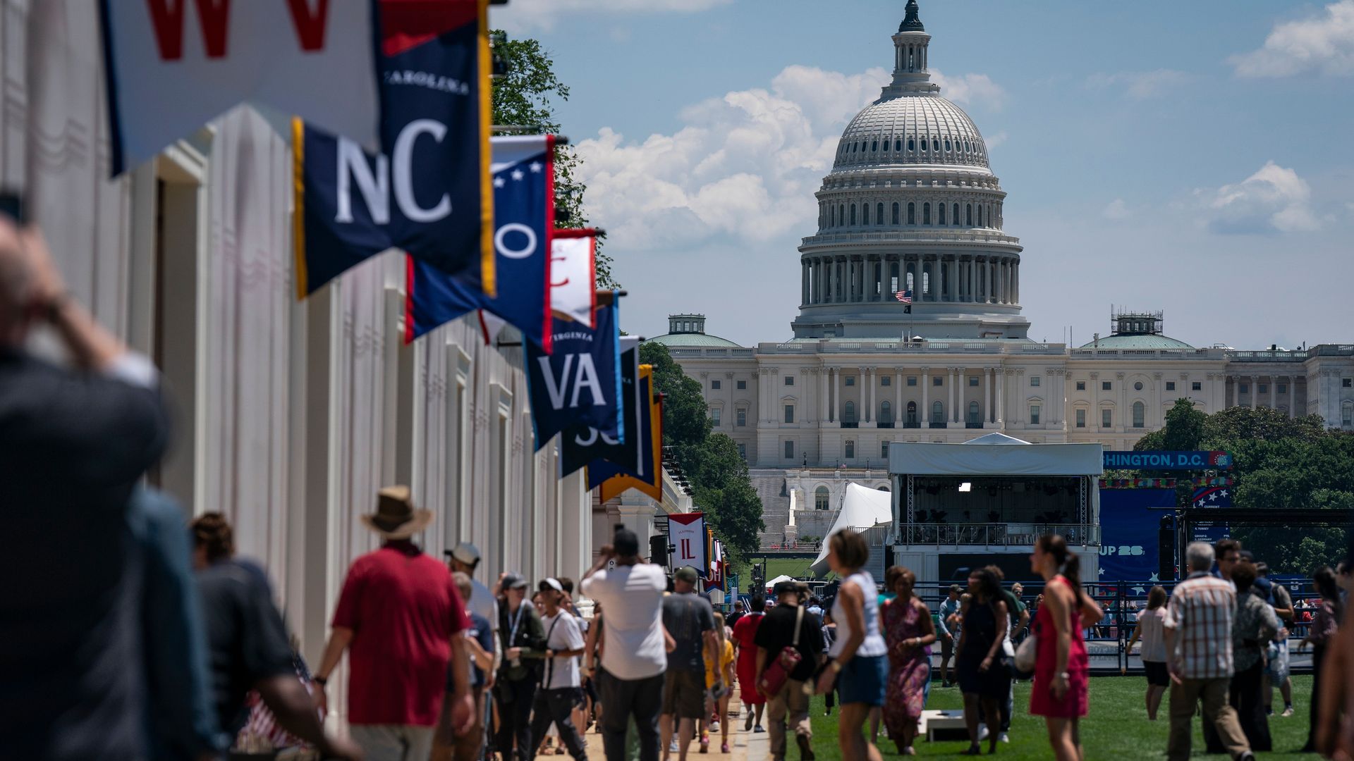 Crowd walking along a sunlit walkway toward the U.S. Capitol, with colorful banners and tents representing U.S. states on the left and the dome of the Capitol in the distance under a blue sky.