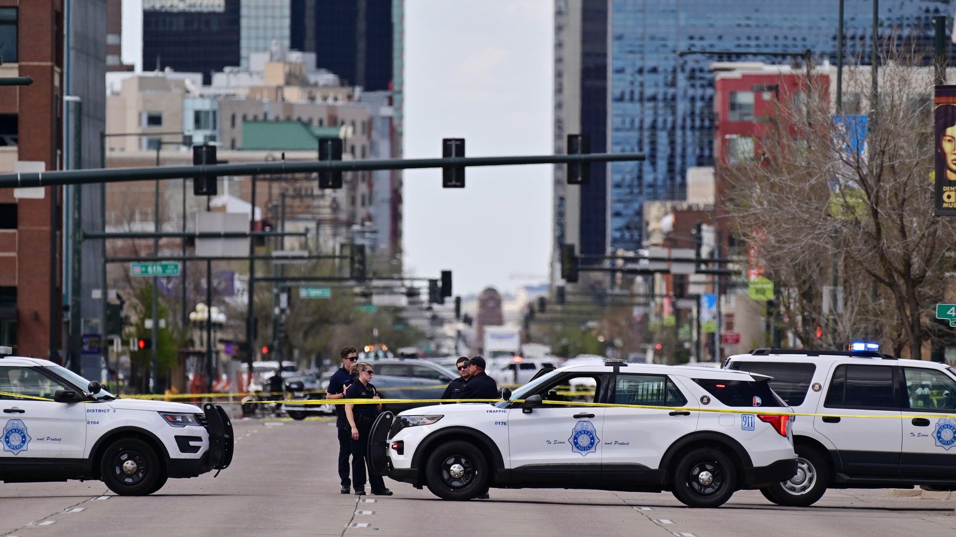 Denver police officers gather around a cruiser behind yellow police tape after a shooting on Broadway near downtown Denver. 