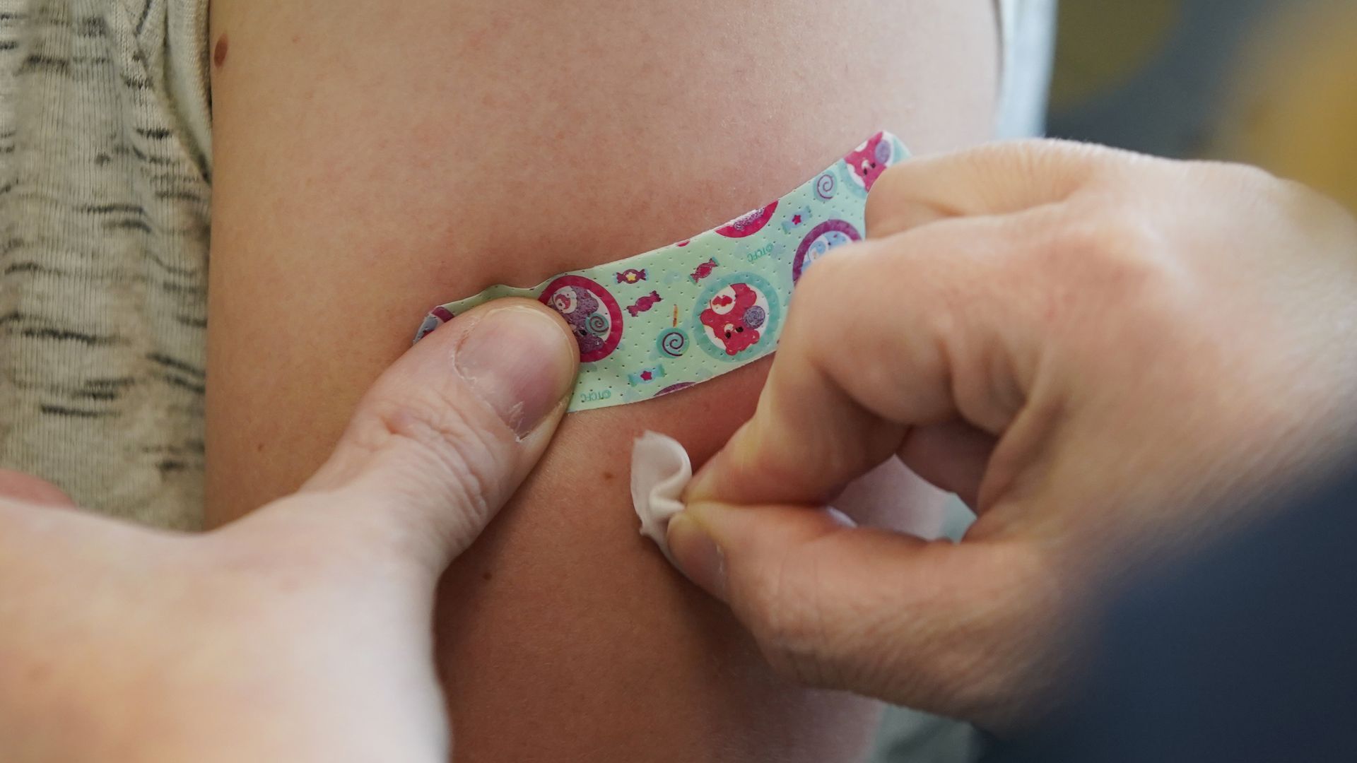 An arm is cleaned by a medical professional in preparation for a person getting a vaccine. a band-aid is on standby