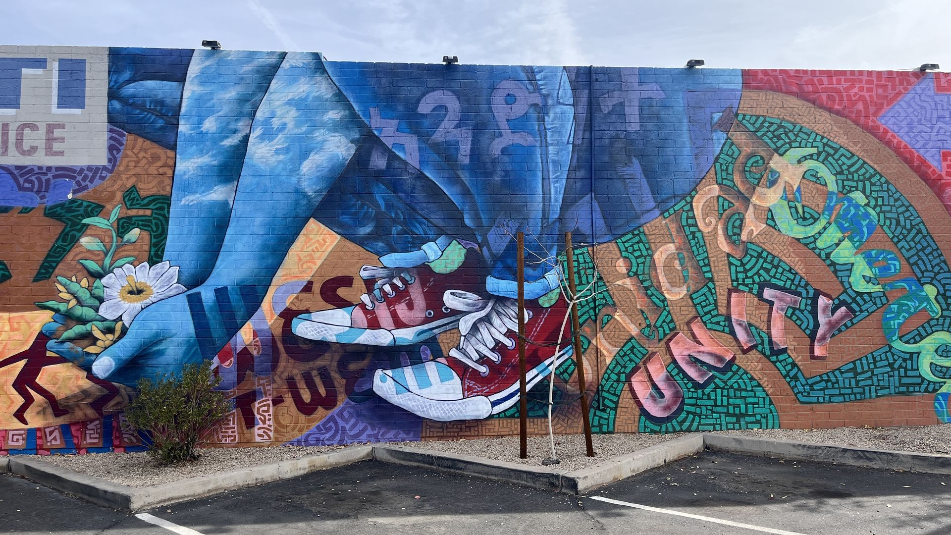 A mural depicting the lower body of a person who is squatting while tending to a flower growing in the ground. The person has a blue body and is wearing red sneakers. 