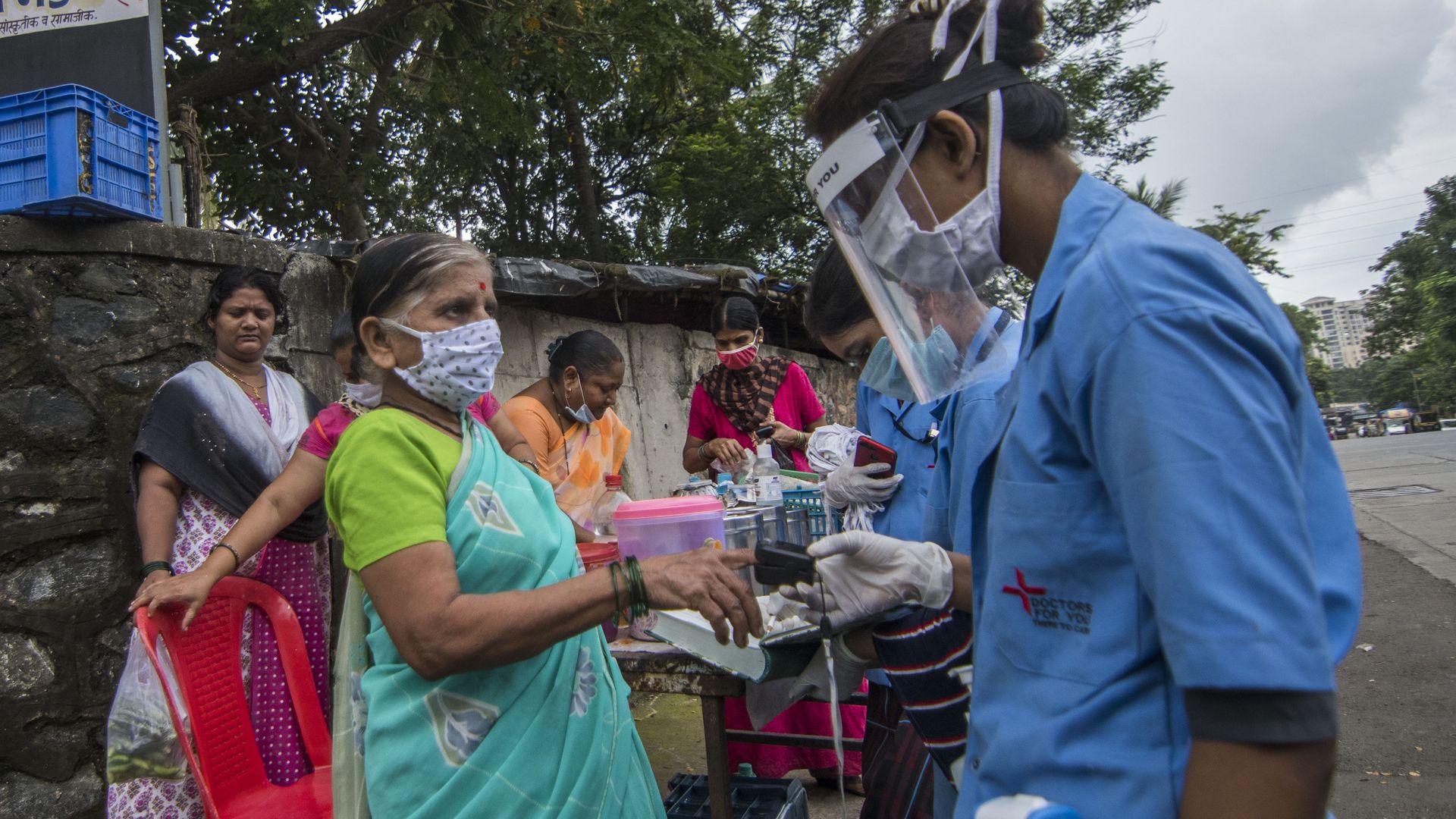 A man wearing a face shield gives a COVID test to a woman wearing a green sari 