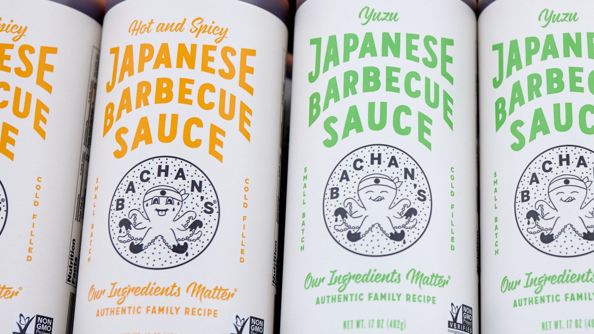 Bottles of Japanese barbecue sauce with white labels; some say Hot and Spicy in orange and others say Yuzu in green. Labels include an octopus logo and Non-GMO Project verified seal.
