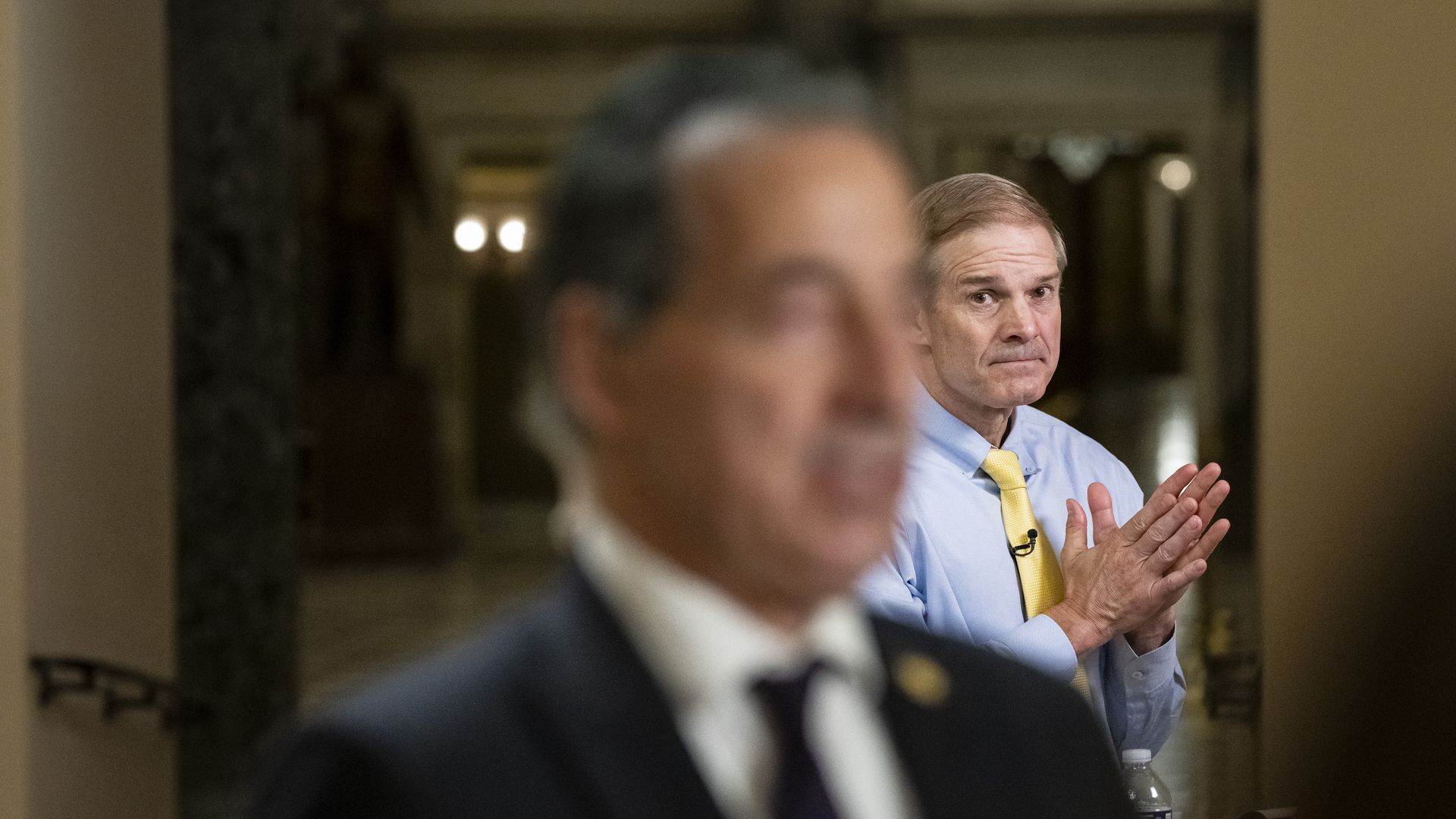 Reps. Jamie Raskin and Jim Jordan speaking into TV cameras in a white and marble hallway.