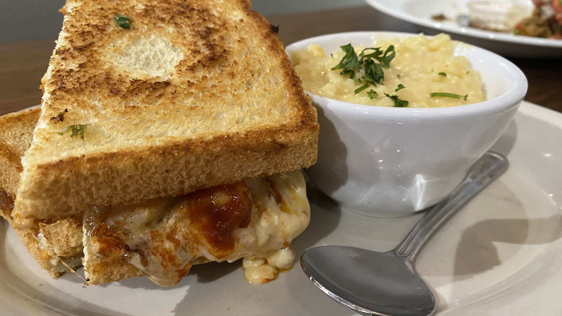 A plate with a grilled sandwich and bowl of cheesy grits. 