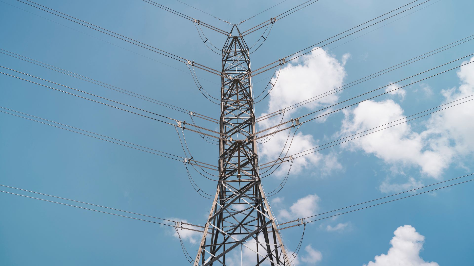 A photo of power transmission lines against a blue sky with a few clouds