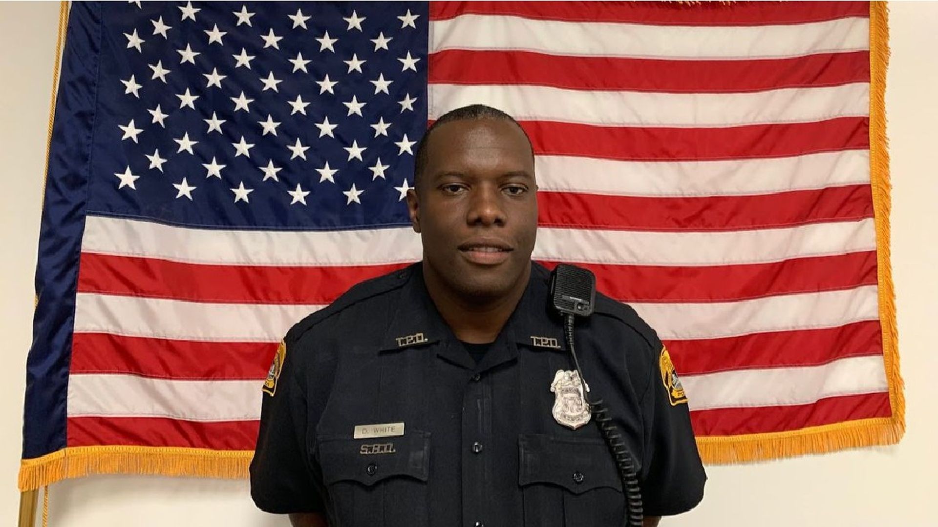 Former Tampa police officer Delvin White stands in uniform in front of an American flag.