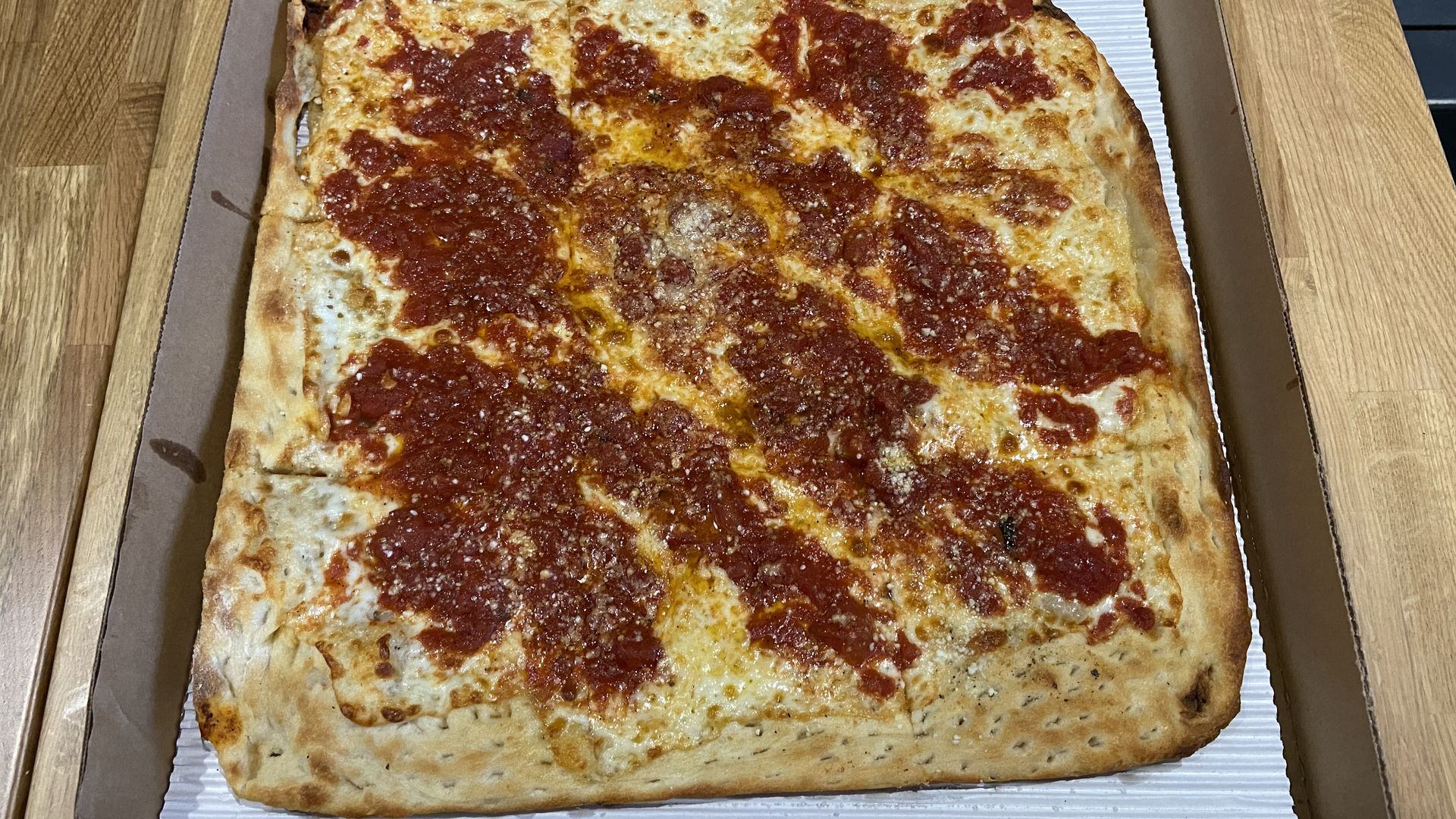 A photo of a square pan-sheet pizza with mozzarella, romano, and marinara in pizza box with the top open
