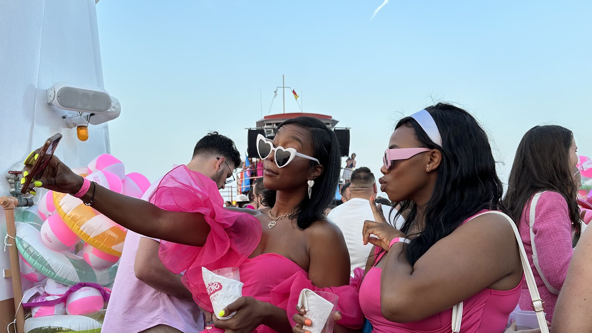 Two stylish Black women in pink dresses take a selfie on the Barbie boat cruise.