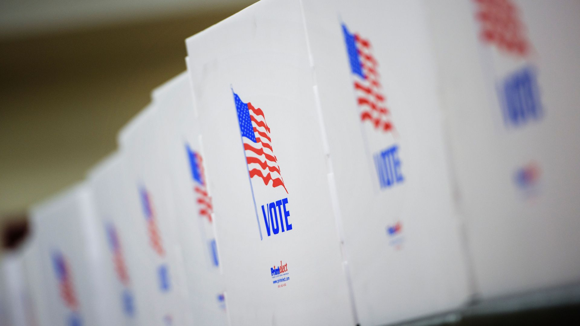 Backs of poll white poll booths are shown diagonally with American flags on them, with word "Vote"