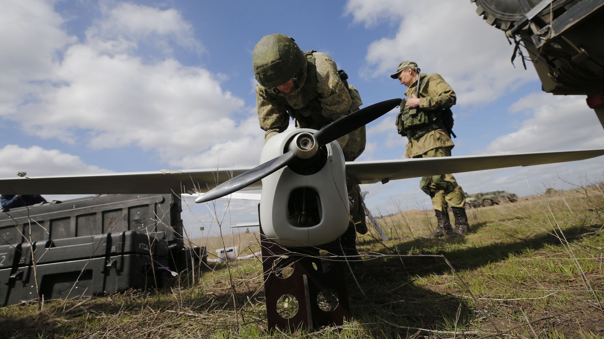 A man in military fatigues bends over a drone on the ground