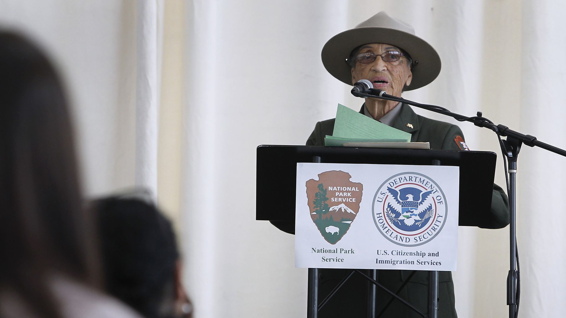 A woman in a ranger hat speaks at a microphone.