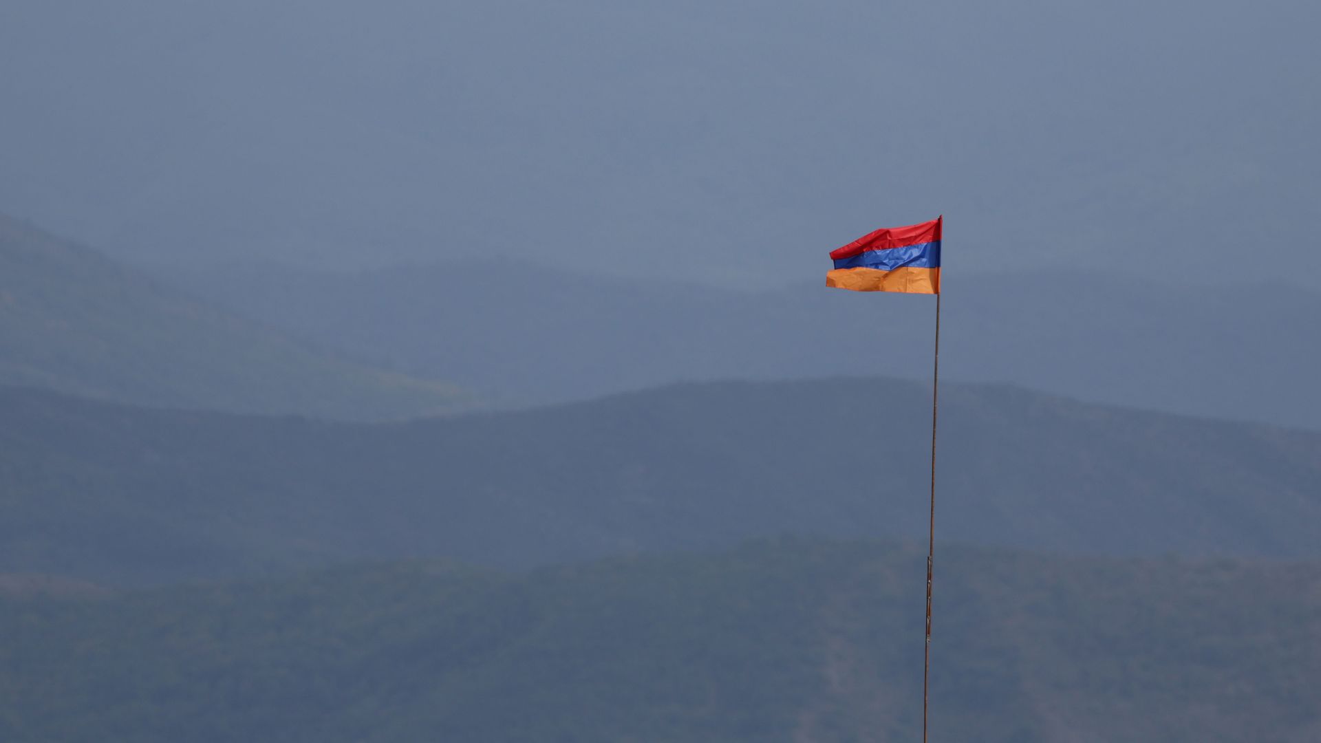 An Armenian flag flutters in the wind. The background is mountainous and dimly lit.