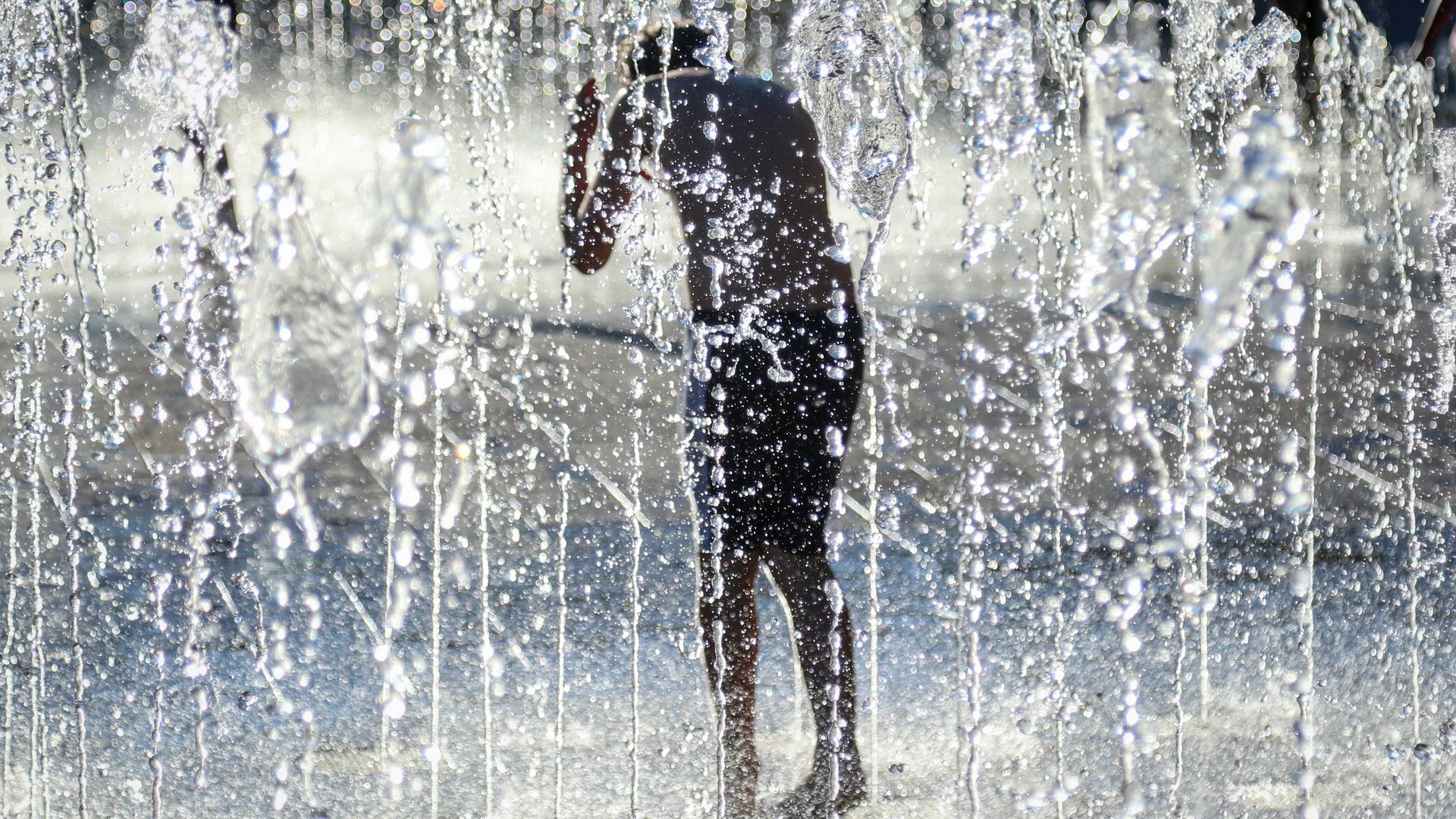 A boy standing in a fountain to keep cool.