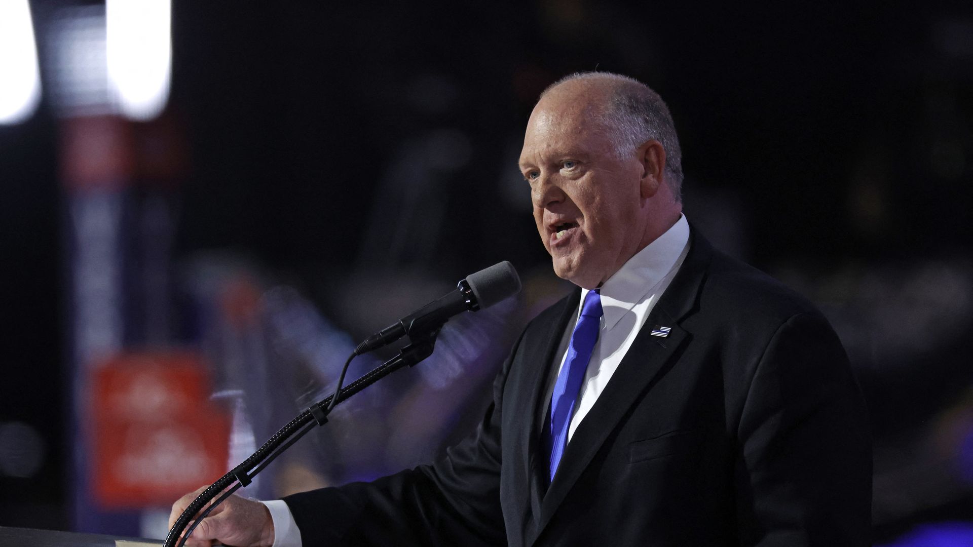 Thomas Homan speaks in front of a black microphone. The camera is facing him from the left. 