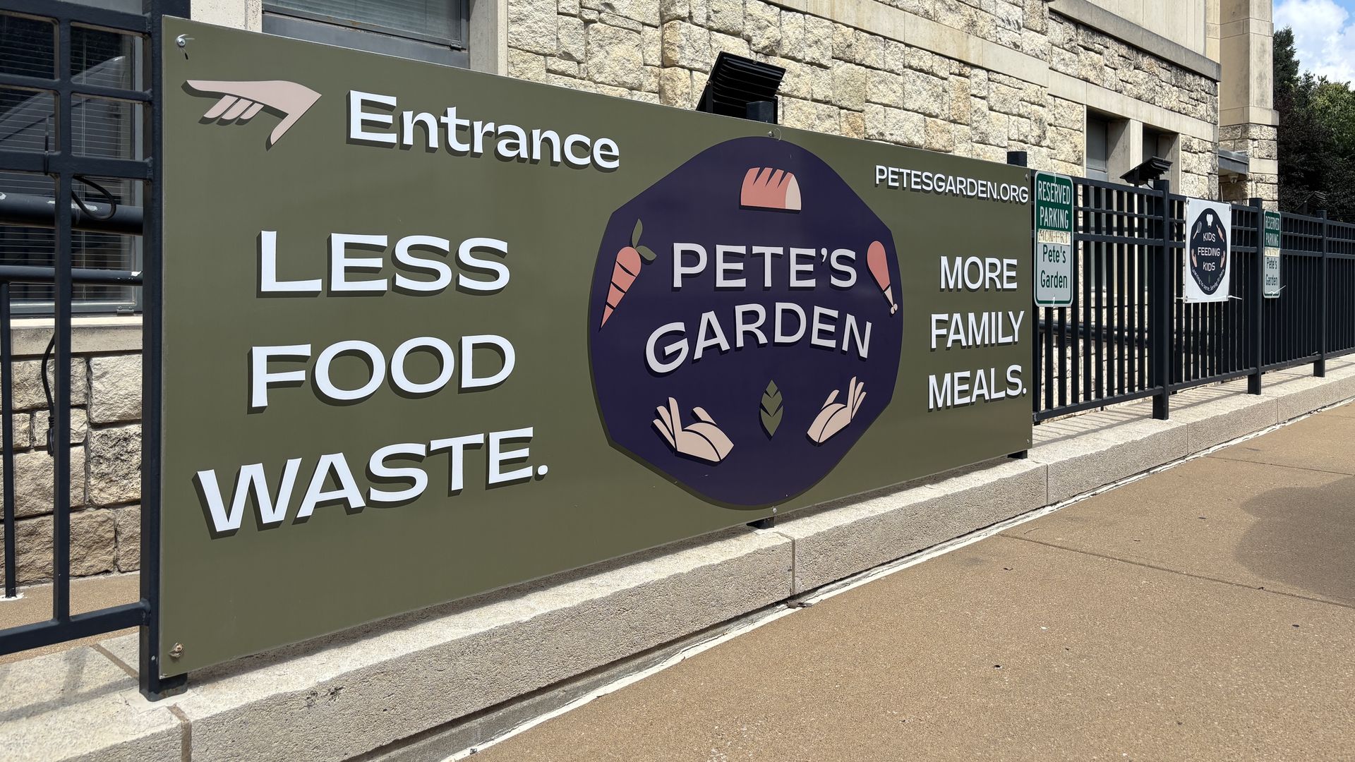 A large outdoor banner on a stone building promoting Pete's Garden: bold white text reads Entrance and Less Food Waste, with a purple circular logo and smaller signs for parking and Kids Feeding Kids on a fence.