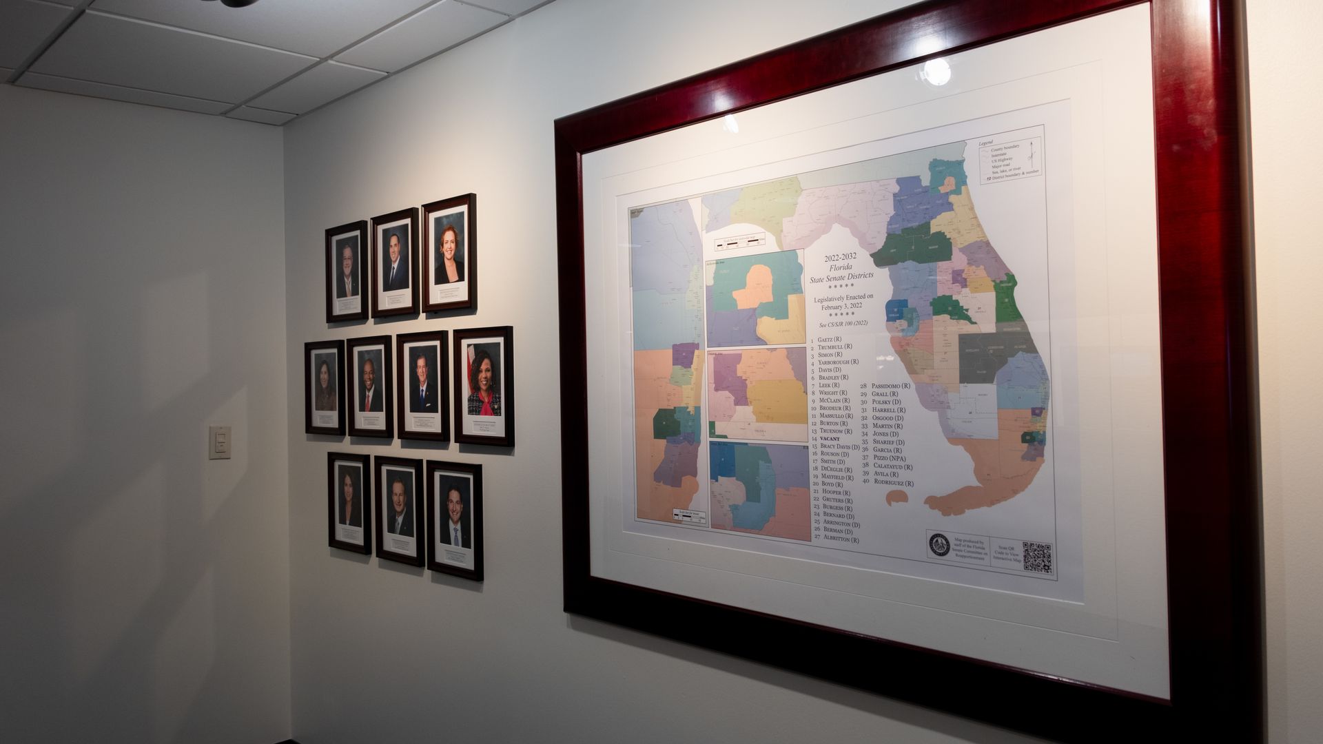 Framed map of Florida’s congressional districts on a wall inside the state Capitol, with smaller framed portraits nearby.