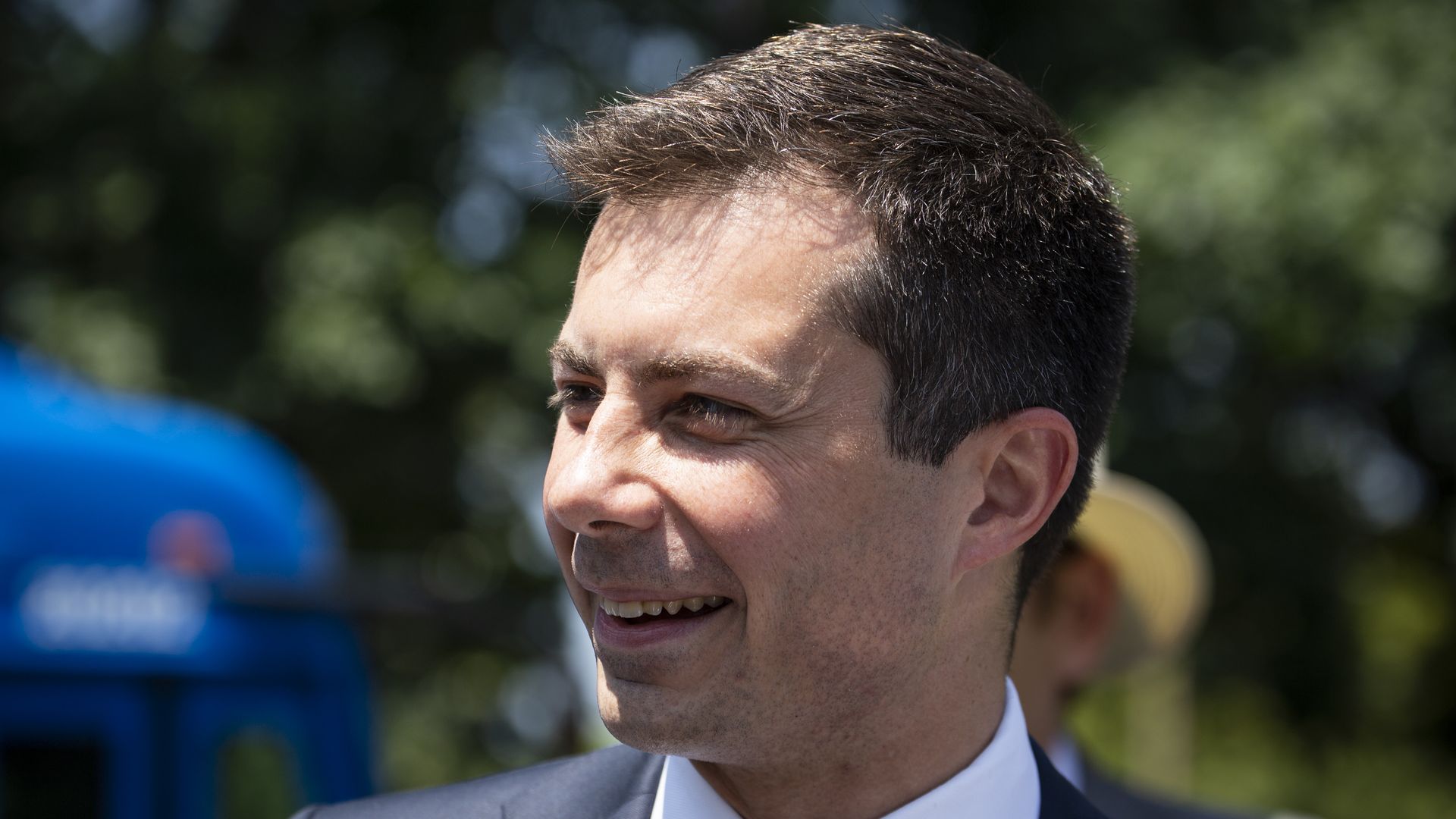 U.S. Transportation Secretary Pete Buttigieg, wearing a blue suit, blue dotted tie and white shirt, smiles as he looks to the right of the camera.