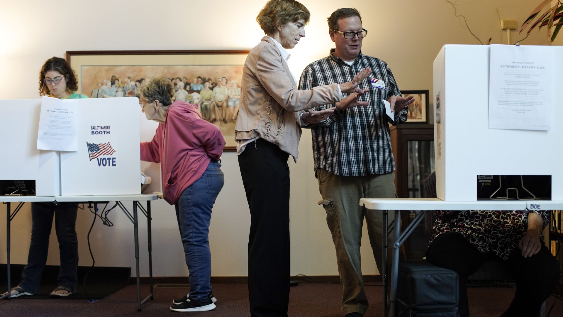 Two standing pollworkers help out a seated person casting a ballot. 