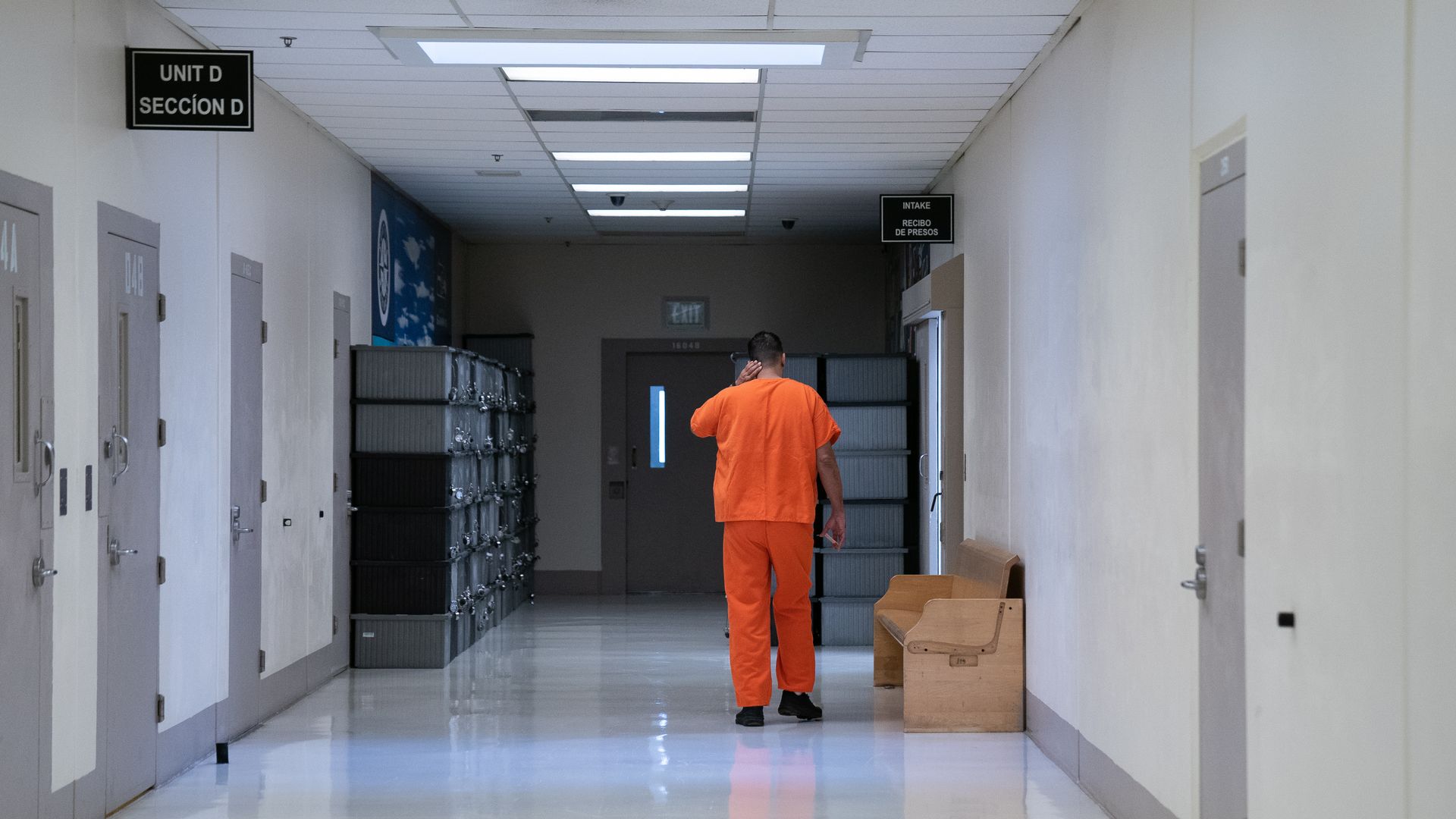 A person wearing an orange shirt and pants walks down a hallway at the Northwest ICE Processing Center.