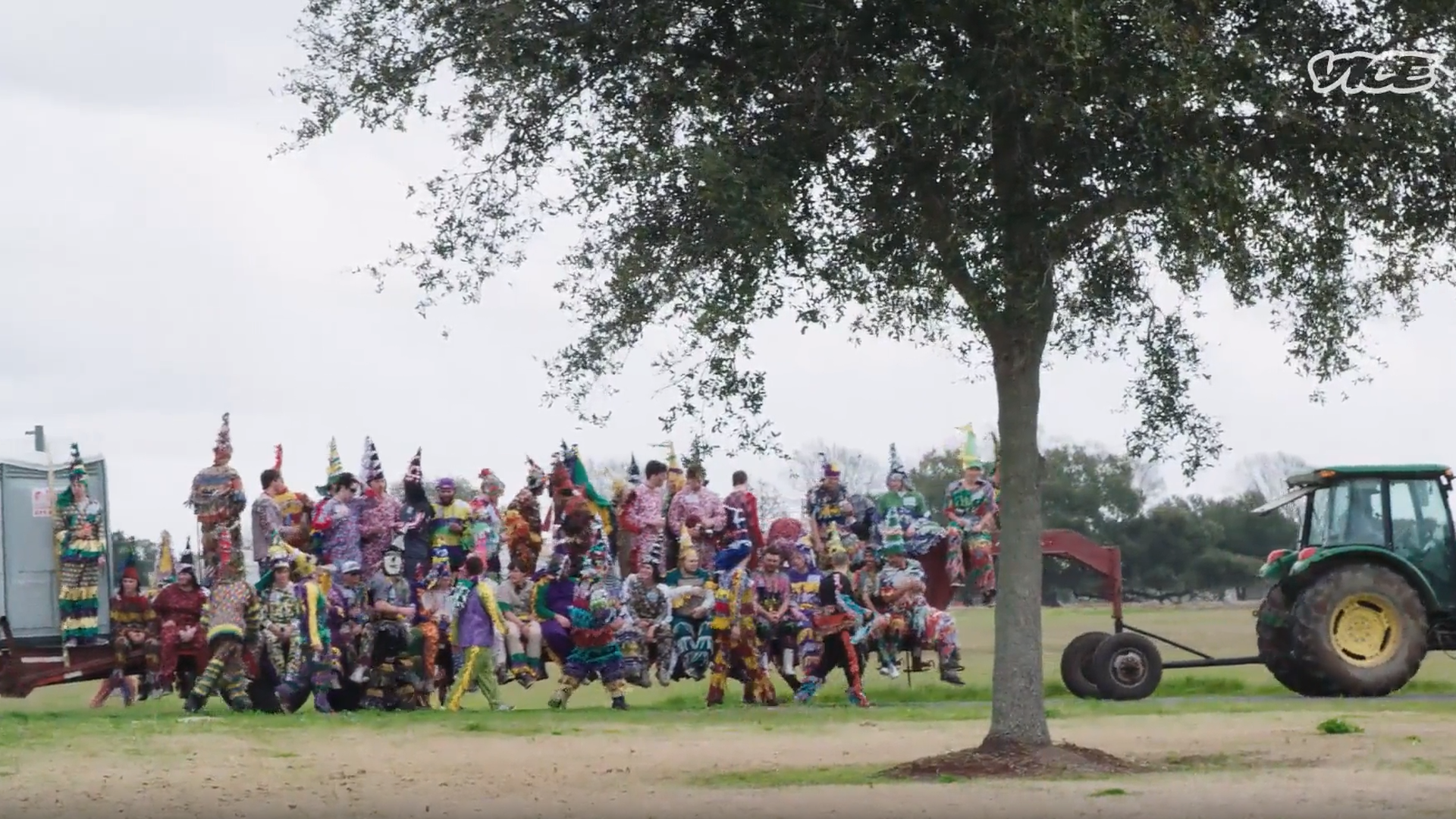 A tractor pulls a trailer that's covered with dozens of Cajun Mardi Gras maskers. There's also a portapotty on the back of the trailer.