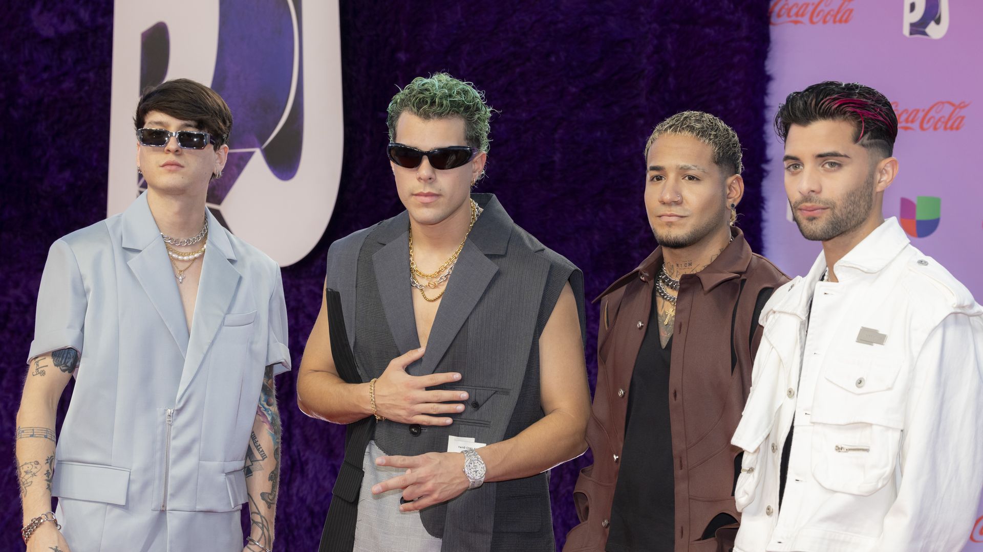 Four men dressed like rock stars stand in front of a purple background