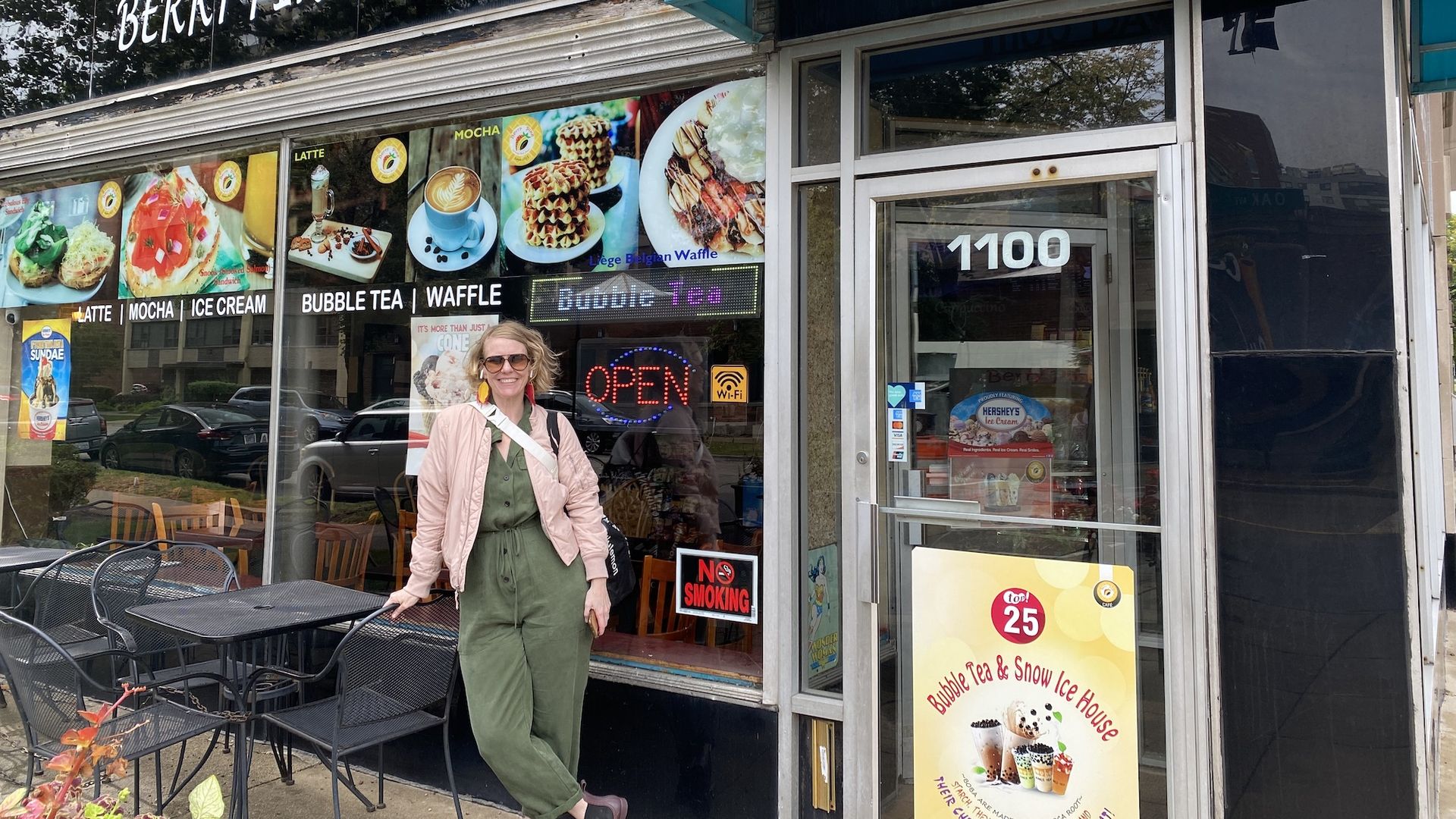 Woman in front of a restaurant window, leaning against a black patio table.