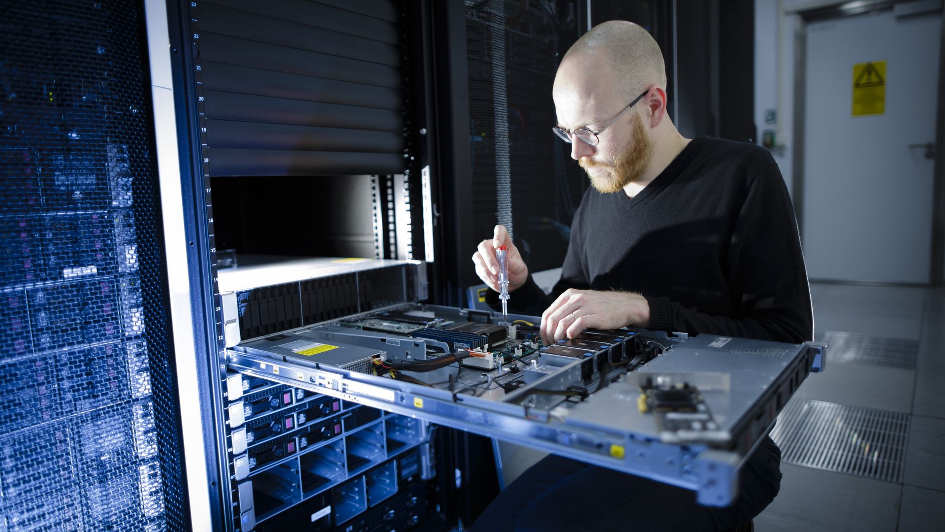 A man unscrews a server part in a data center.