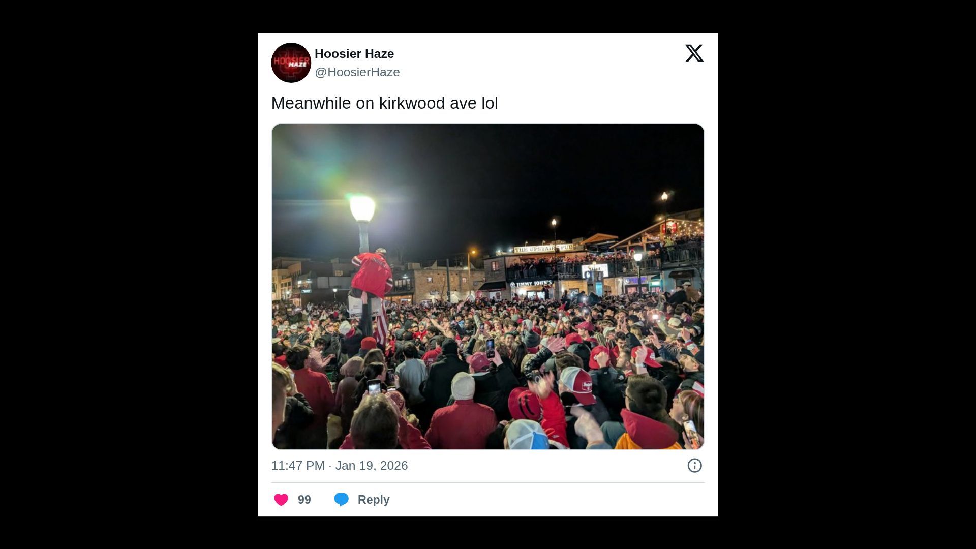 Crowd of people gathered at night on Kirkwood Avenue, many wearing red clothing and hats, with one person climbing a lamp post. Buildings and signs lit in the background.