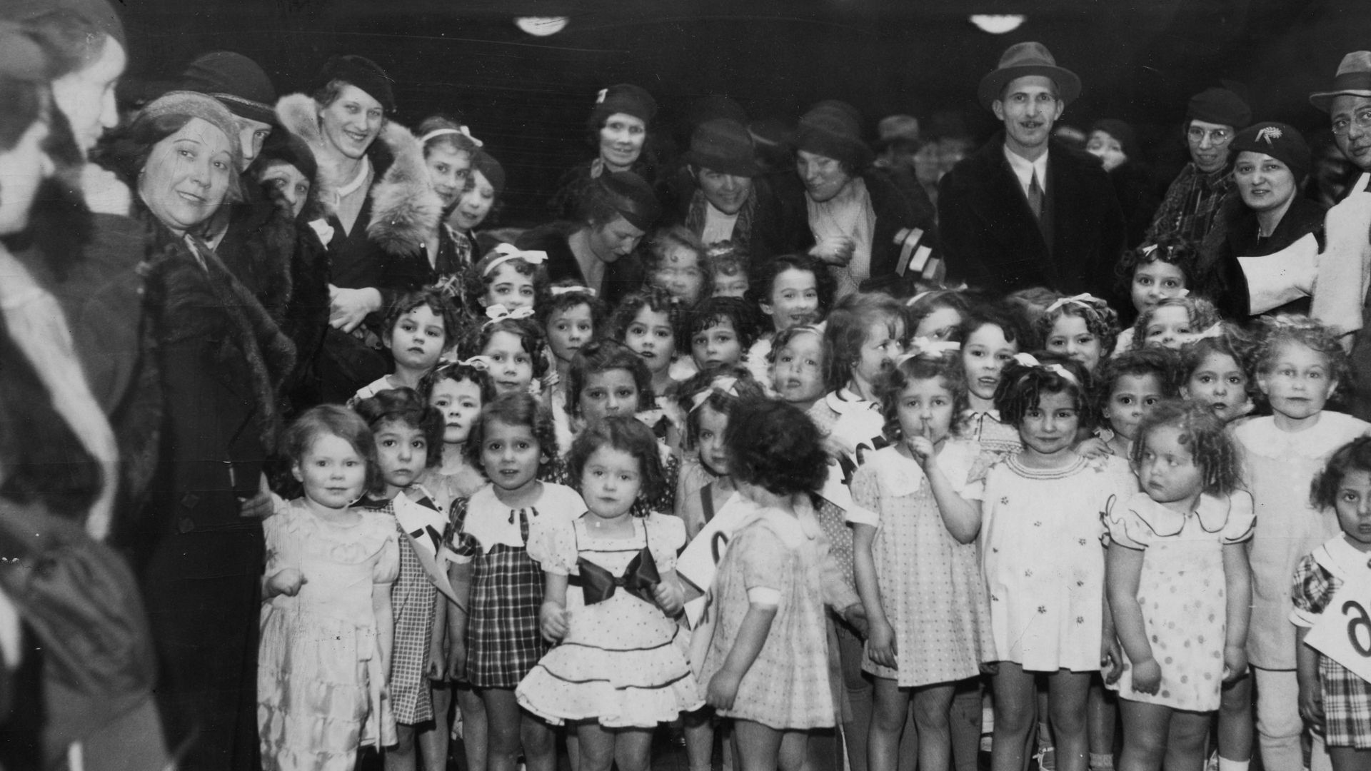 Little girls dressed up as Shirley Temple pose for a photo in 1935 flanked by their parents. 