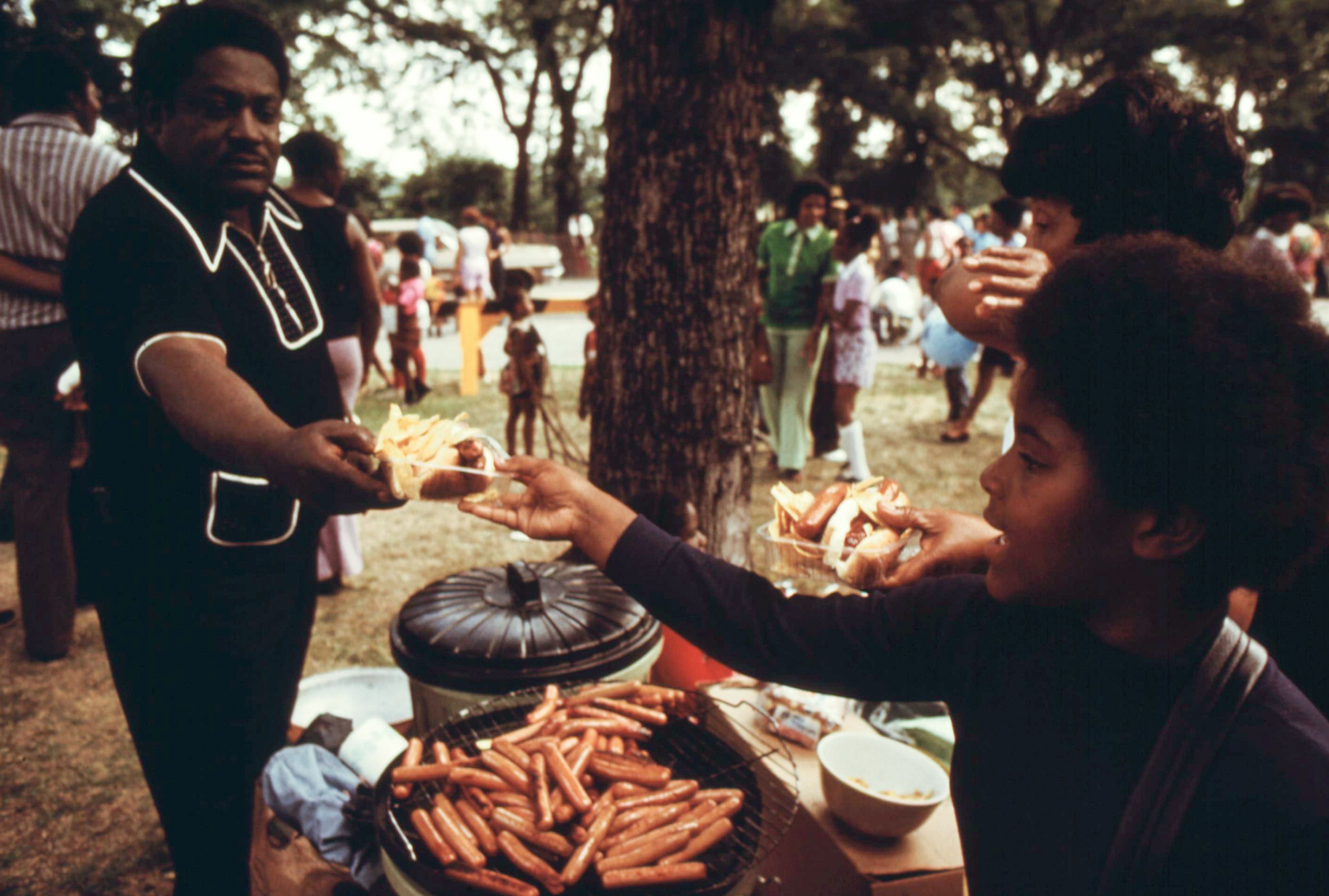 Photo of people eating hot dogs in a park 